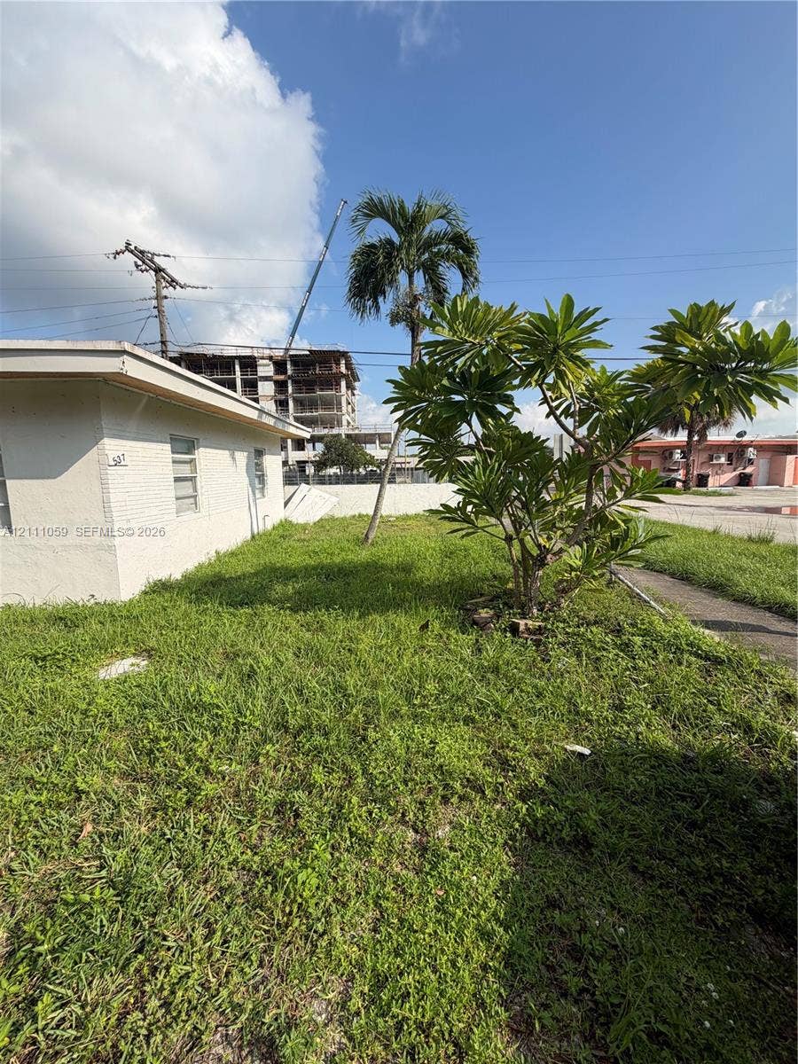 Exterior side elevation featuring masonry wall construction, horizontal jalousie windows, and mature palm vegetation