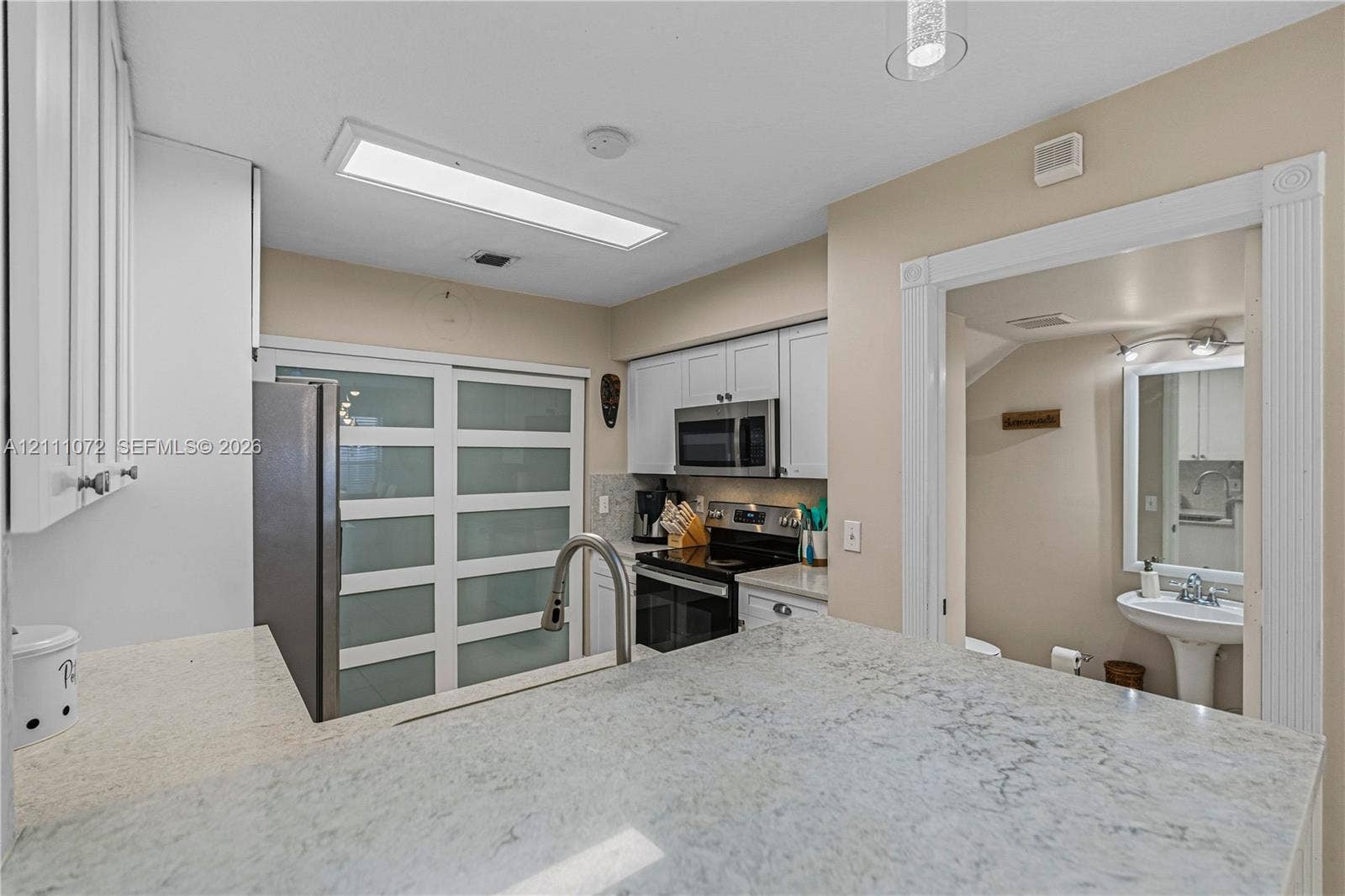 Kitchen featuring stone countertops, white cabinetry, a high-arc faucet, and frosted glass sliding doors, with a pedestal sink in the background