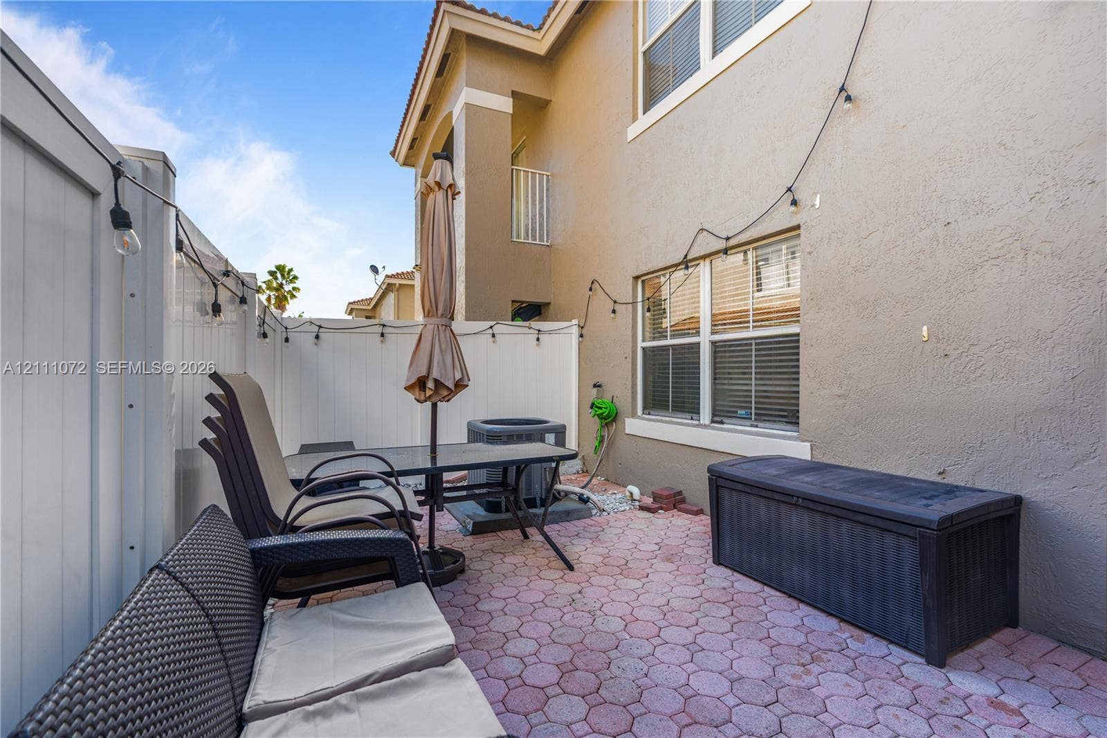 Enclosed patio featuring red concrete pavers, white vinyl privacy fencing, and a multi-story exterior facade with dual-pane windows