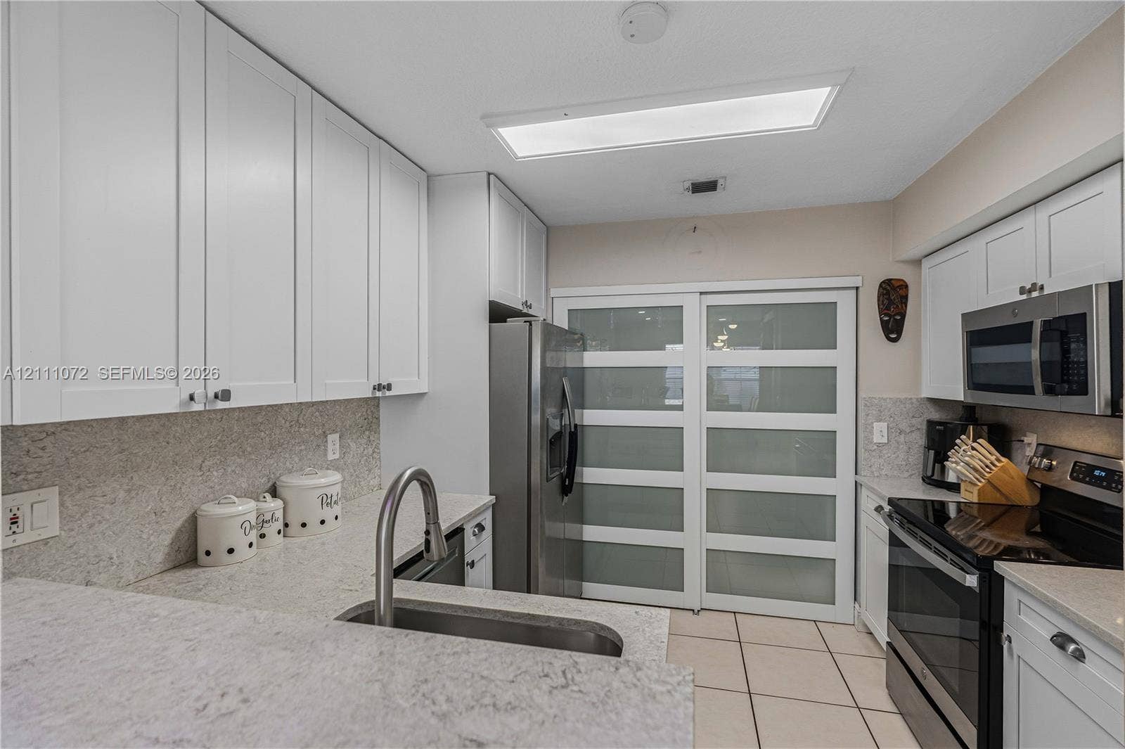 Kitchen featuring white shaker-style cabinetry, stone-finish countertops, stainless steel appliances, a high-arc pull-down faucet, and frosted glass sliding panels