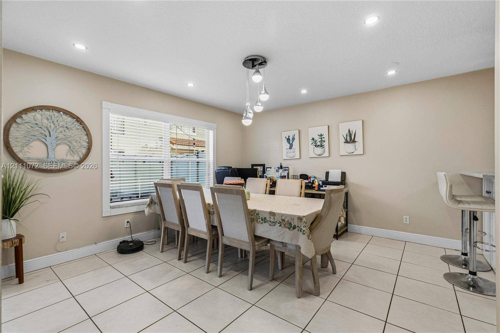 Open-concept room featuring light-toned tile flooring, recessed ceiling lighting, a multi-pendant light fixture, and a large window with horizontal blinds