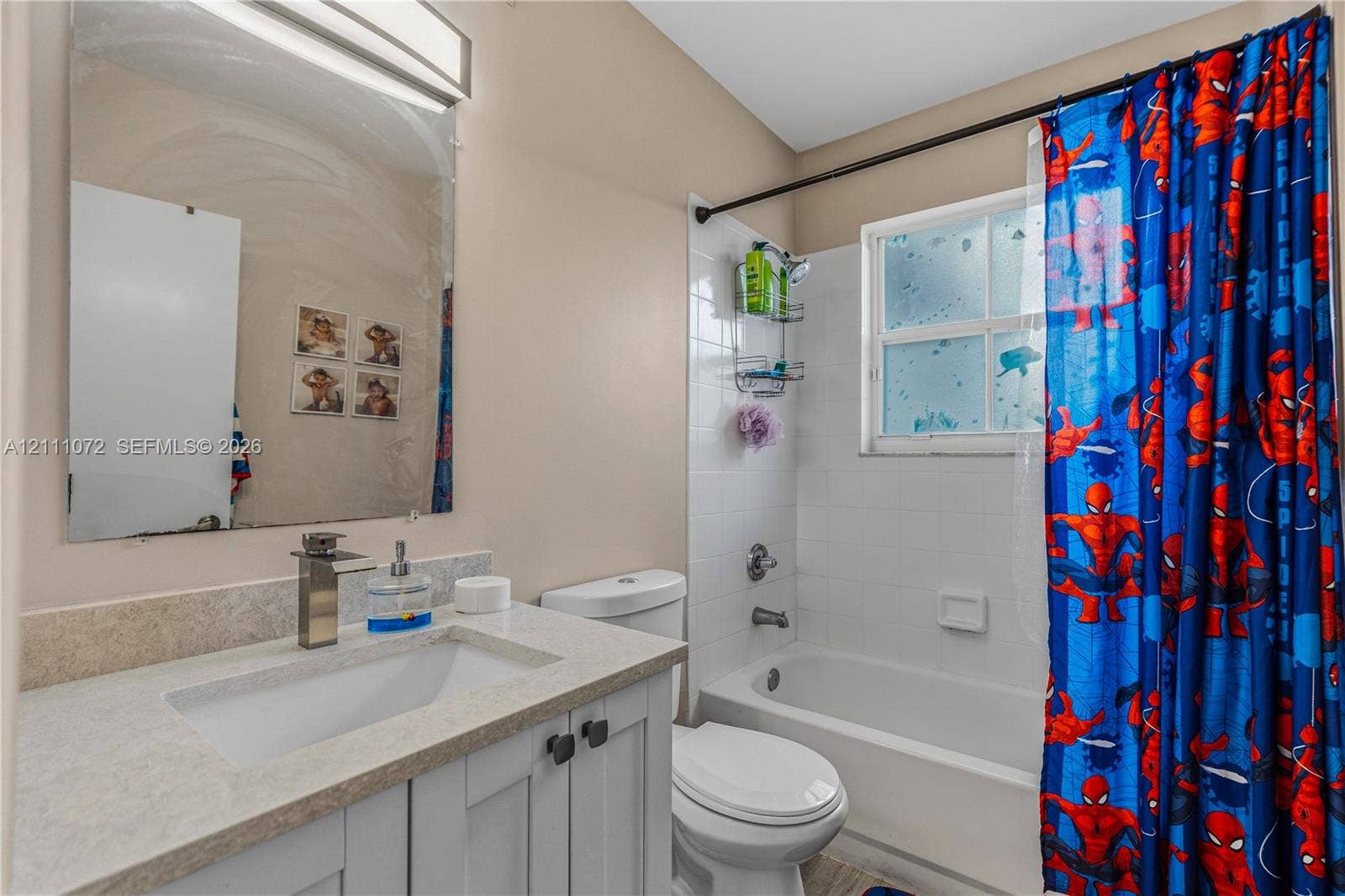 Bathroom featuring a white vanity cabinet with a stone-surface countertop, an integrated rectangular sink, a tall single-handle faucet, a wall-mounted mirror with integrated lighting, and a tub-shower combination with white tile surround