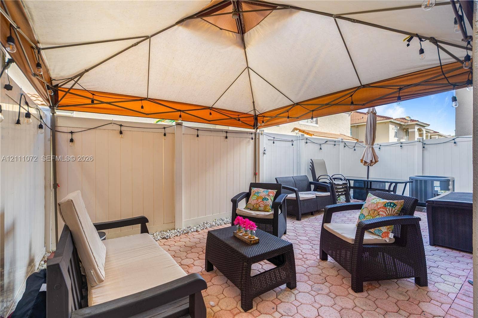 Outdoor patio featuring red-toned stone pavers, a white vinyl privacy fence, and a built-in frame structure
