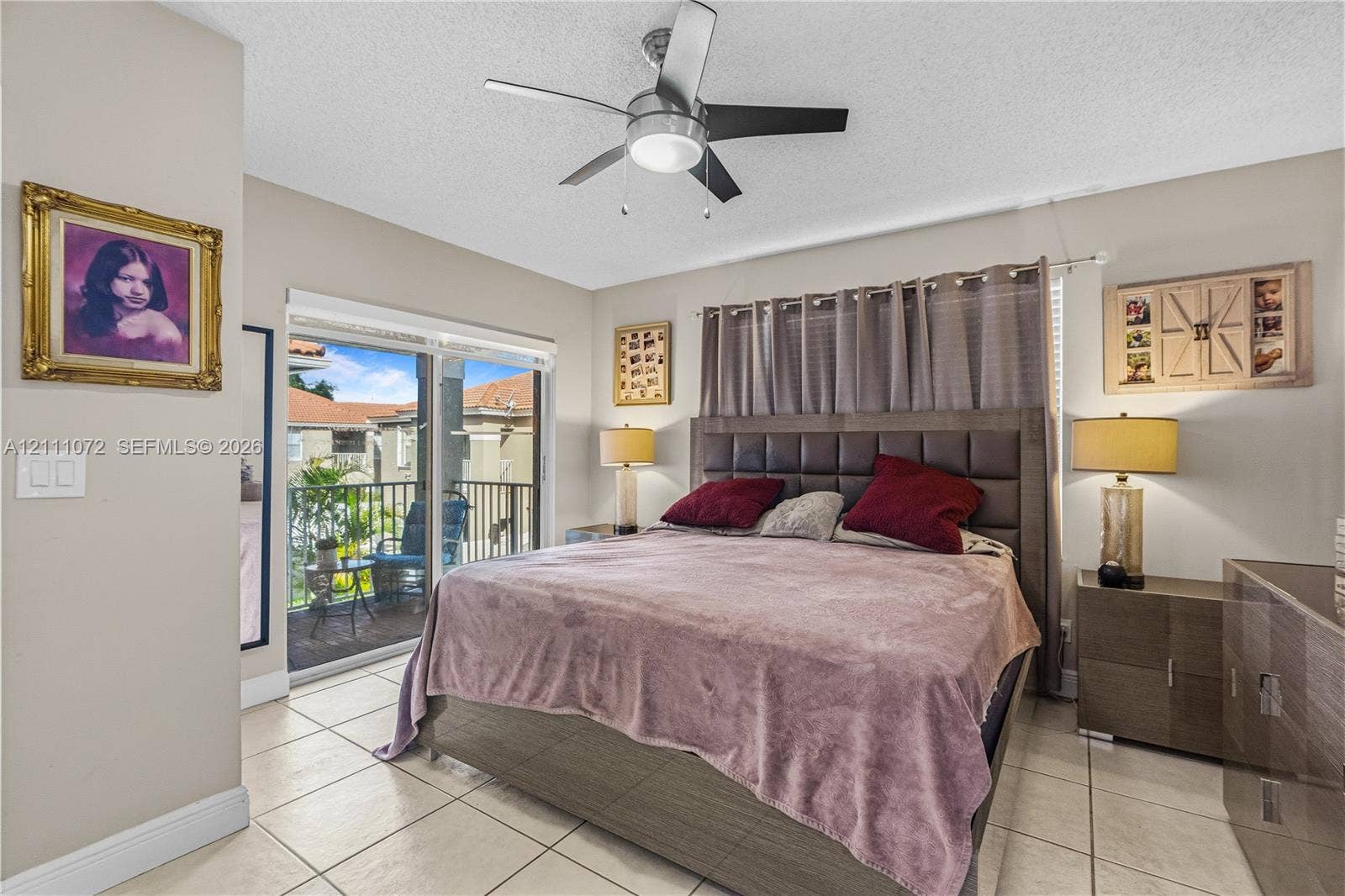 Neutral-toned interior featuring large-format tile flooring, a multi-blade ceiling fan with integrated lighting, and sliding glass doors providing outdoor access to a balcony with metal railing