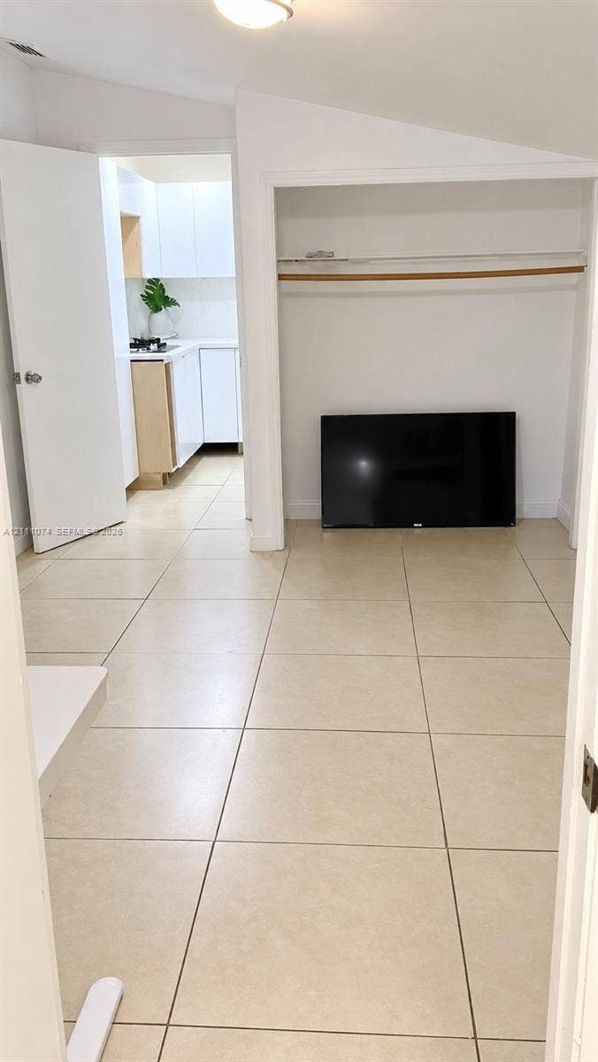 Interior space featuring large-format ceramic tile flooring, a recessed closet with a built-in hanging rod, and a vaulted ceiling