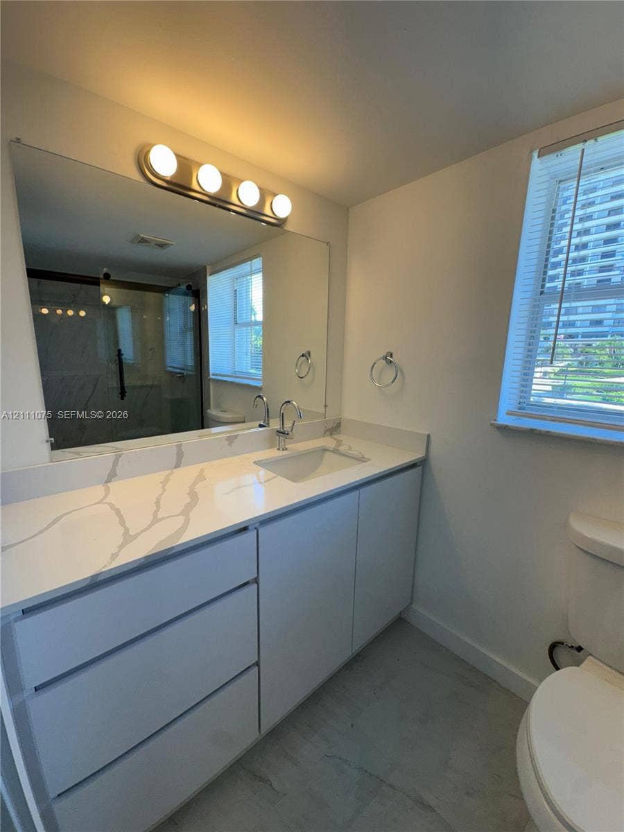 2318 NE 7th Street, #34, Hallandale Beach, Hallandale Beach, FL 33009 Bathroom featuring a vanity with a white-veined stone countertop, an integrated rectangular sink, wall-to-wall mirror, four-bulb vanity lighting, and a walk-in shower with glass enclosure