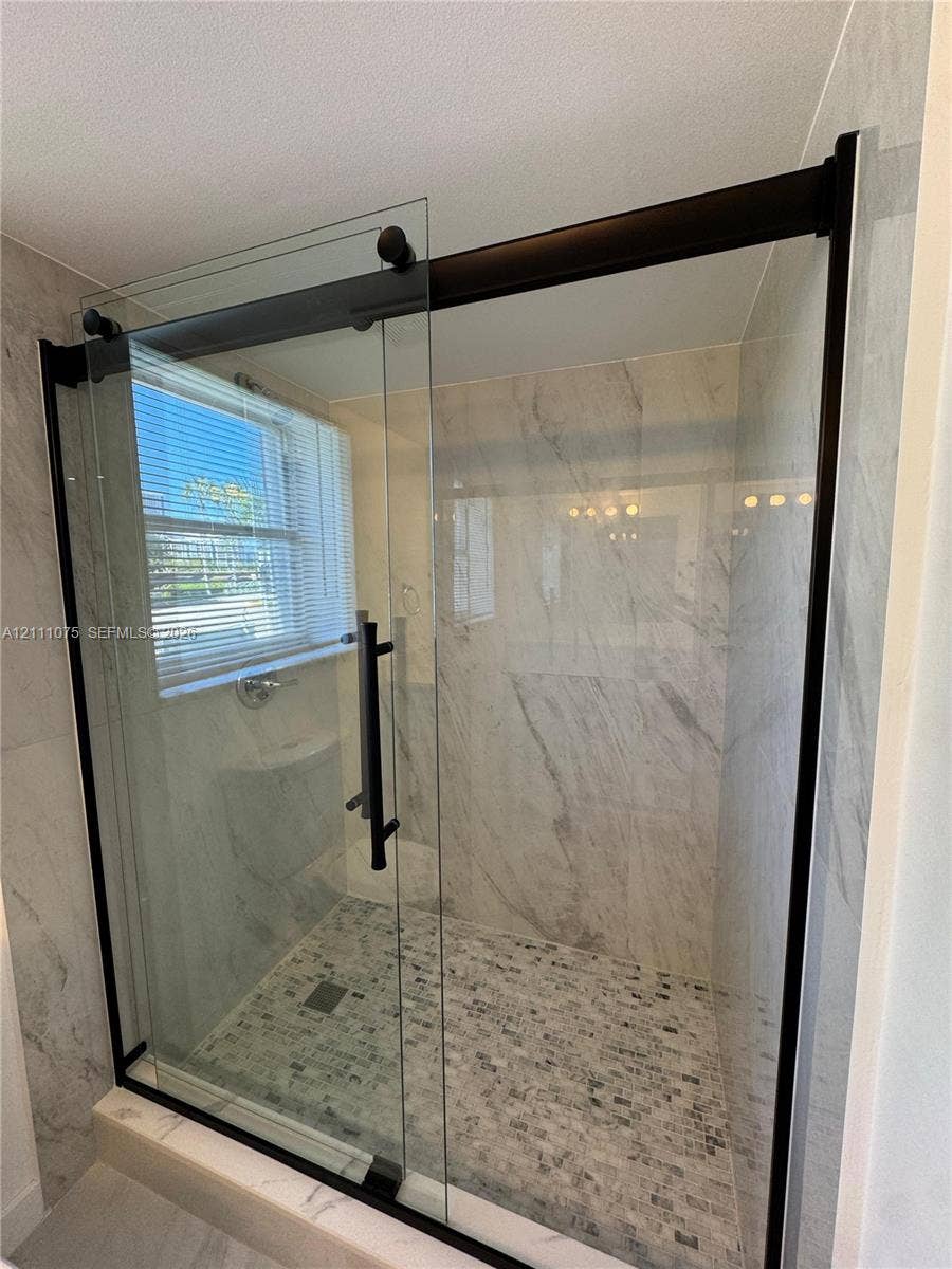 2318 NE 7th Street, #34, Hallandale Beach, Hallandale Beach, FL 33009 Walk-in shower featuring a sliding glass door with matte black hardware, stone-finish wall tile, and mosaic tile flooring