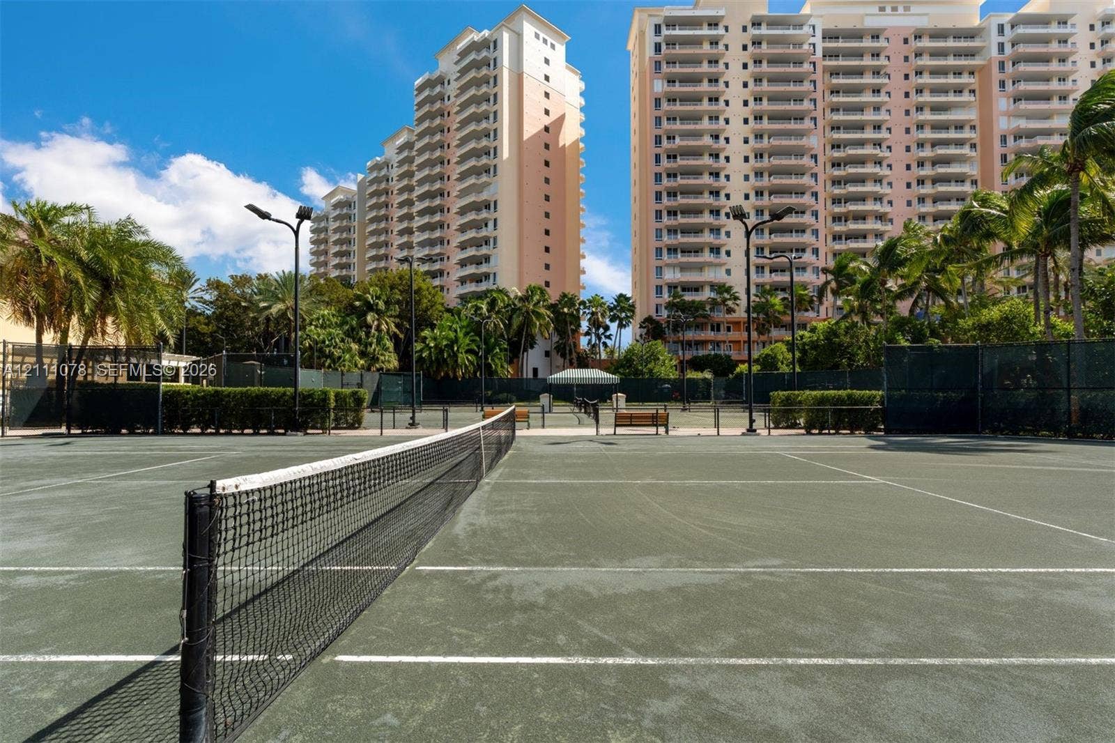 765 Crandon Boulevard, #311, Key Biscayne, FL 33149 Tennis court featuring a synthetic surface, perimeter fencing, overhead lighting, and benches