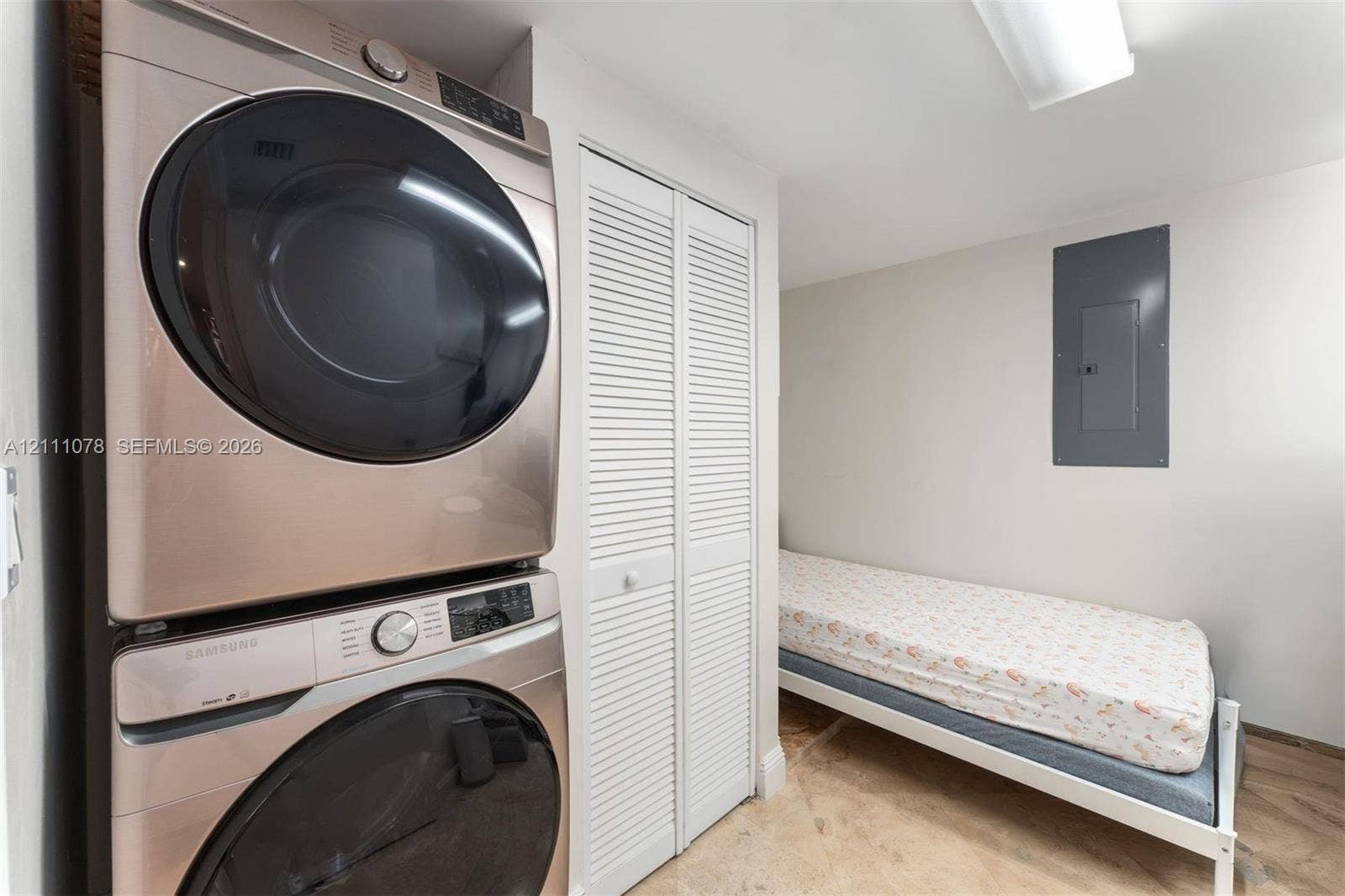 765 Crandon Boulevard, #311, Key Biscayne, FL 33149 Laundry area featuring a stacked stainless steel front-load washer and dryer set, bifold louvered doors, and stone-finish flooring
