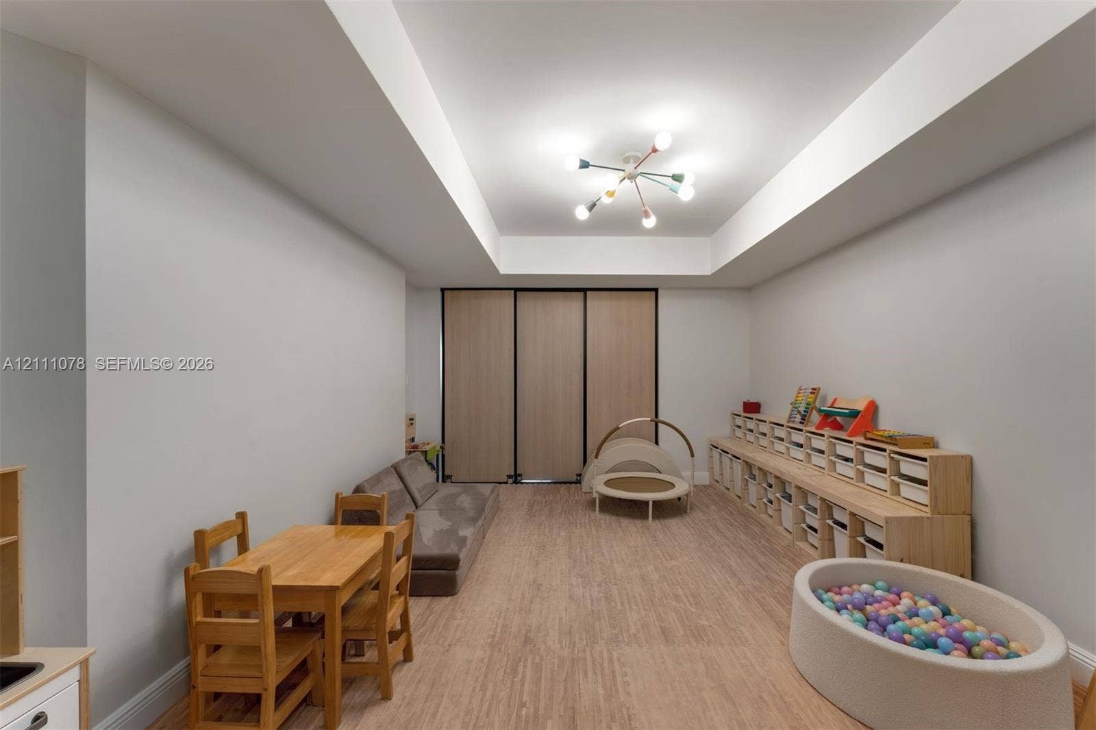 765 Crandon Boulevard, #311, Key Biscayne, FL 33149 Interior space featuring a recessed tray ceiling, multi-arm light fixture, and wood-finish flooring, accented by floor-to-ceiling built-in wooden storage cabinetry and sleek folding partition doors