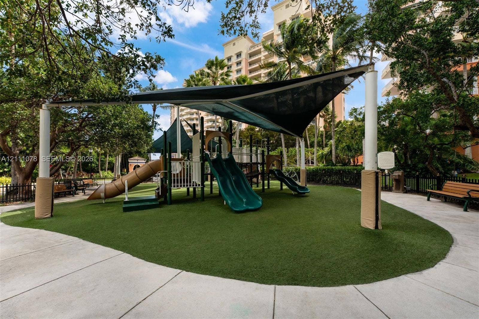 765 Crandon Boulevard, #311, Key Biscayne, FL 33149 Recreational area featuring a playground structure with multiple slides, synthetic turf surfacing, a canopy shade sail, and surrounding concrete pathways