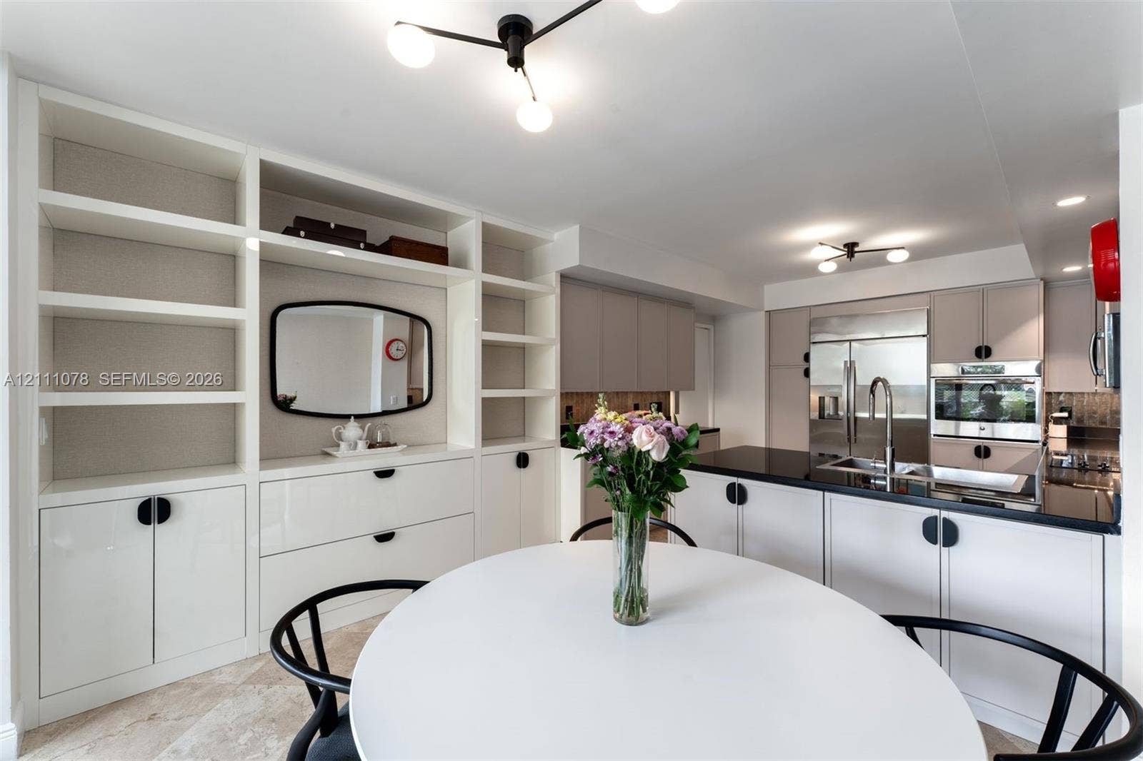 765 Crandon Boulevard, #311, Key Biscayne, FL 33149 Custom built-in white cabinetry with open shelving, sleek flat-panel kitchen cabinetry, polished dark countertops, stainless steel appliances, and contemporary multi-arm light fixtures