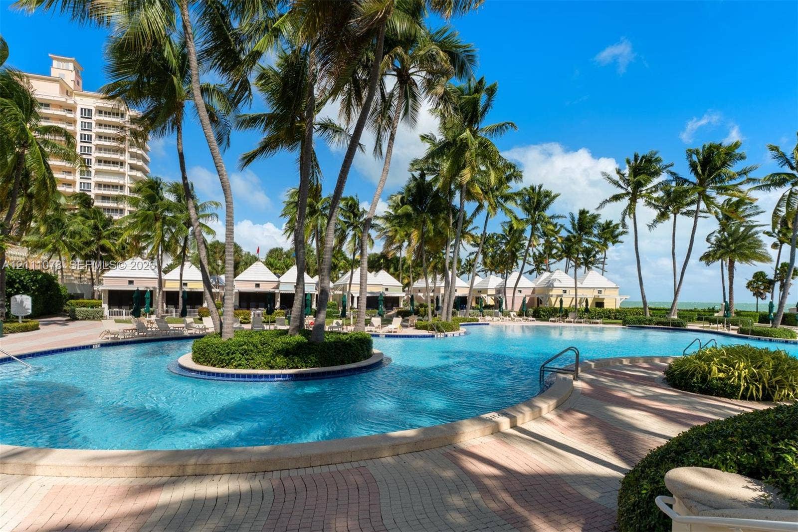 765 Crandon Boulevard, #311, Key Biscayne, FL 33149 Resort-style swimming pool featuring a central island with mature palm trees, multi-tone paver decking, and cabanas