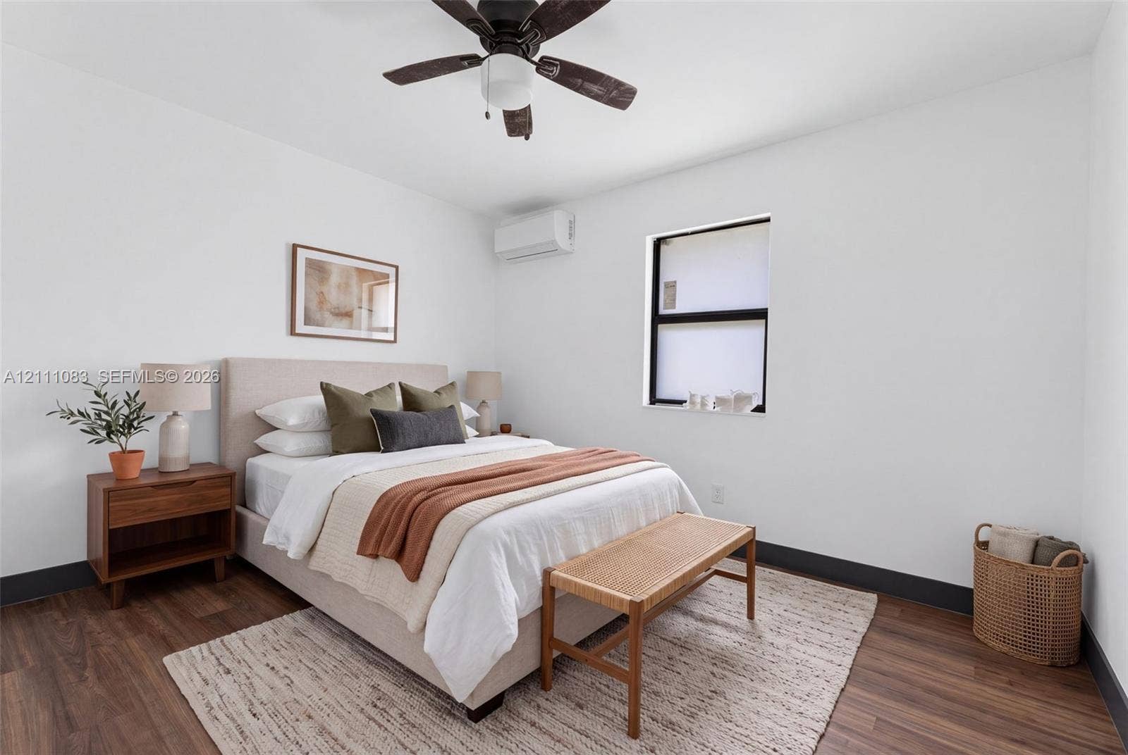 Room featuring wood-finish flooring, a wall-mounted ductless air conditioning unit, a ceiling fan, and a window with a black frame