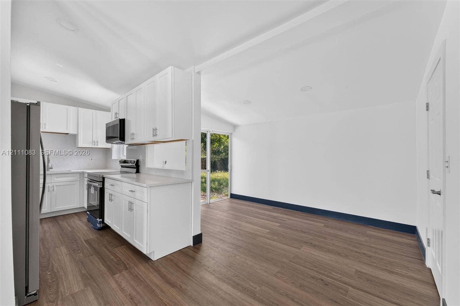 Kitchen featuring white cabinetry, solid-surface countertops, integrated stainless steel appliances, and wood-finish flooring with sliding glass doors