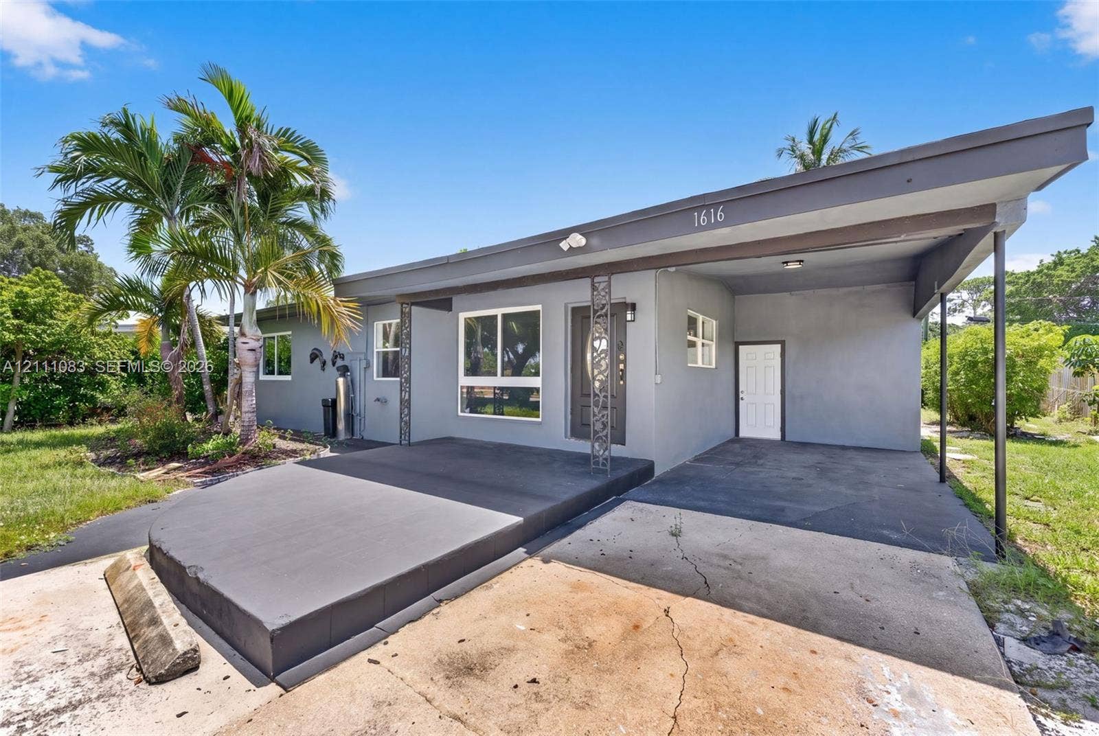 Mid-century modern exterior featuring a flat roofline, attached covered carport, decorative metal porch pillars, and a concrete patio
