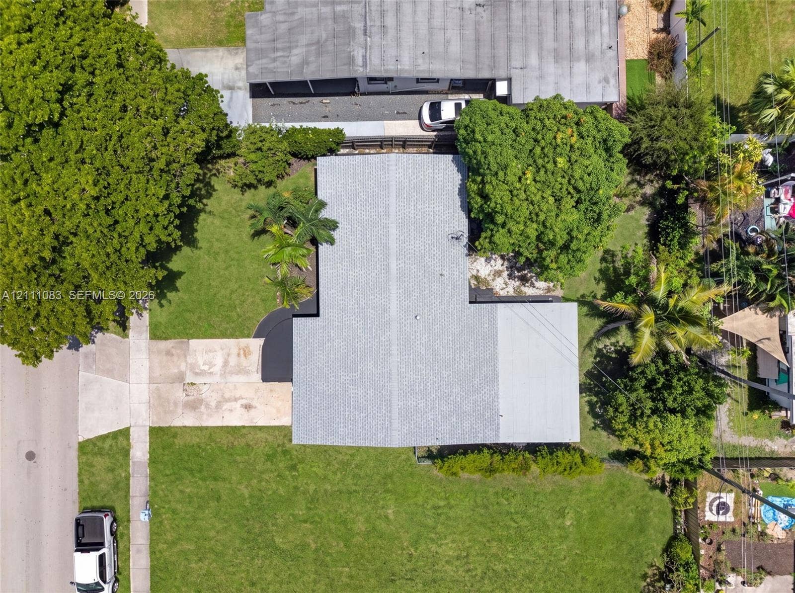 Aerial view featuring a paved driveway, expansive lawn, mature tree canopy, and established landscaping