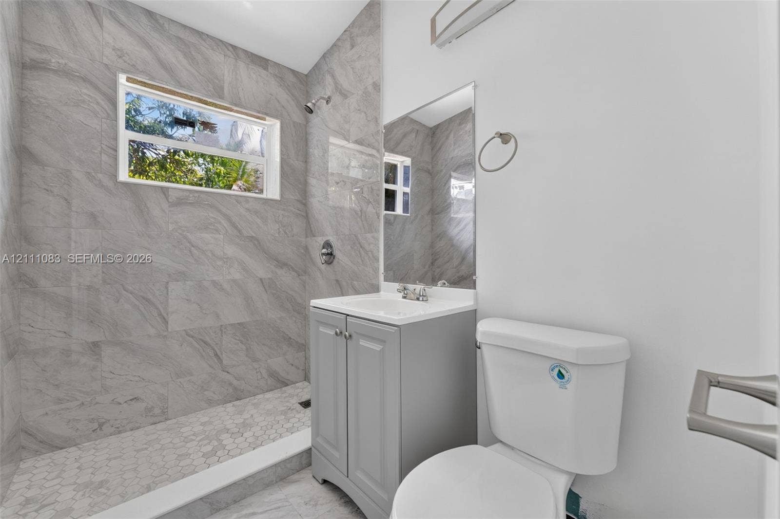 Bathroom featuring floor-to-ceiling gray tile shower walls, hexagonal tile shower flooring, and a grey single-sink vanity