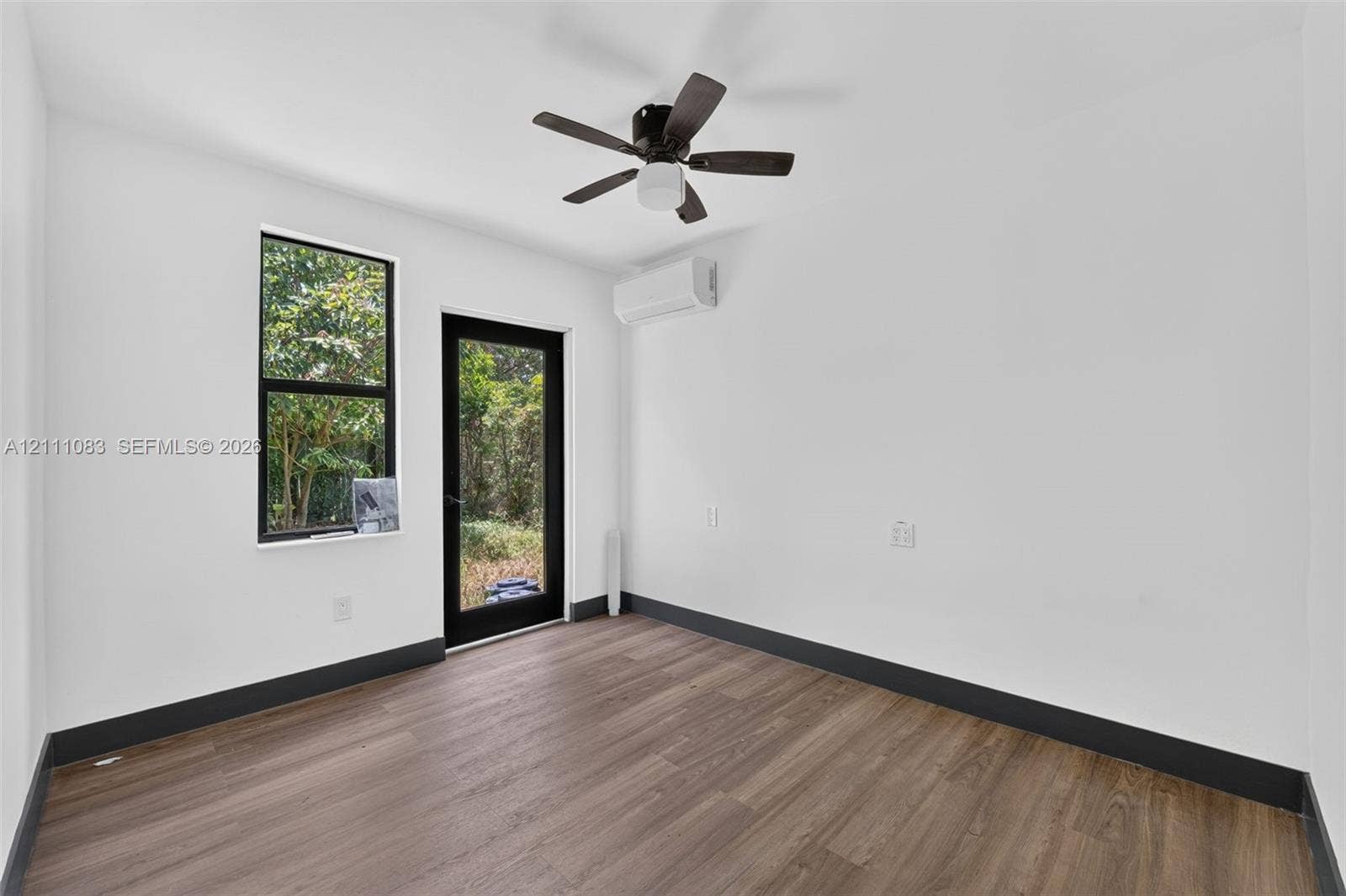 Interior room featuring wood-finish flooring, a wall-mounted ductless mini-split system, a ceiling fan with integrated lighting, and a glass-paneled exterior door