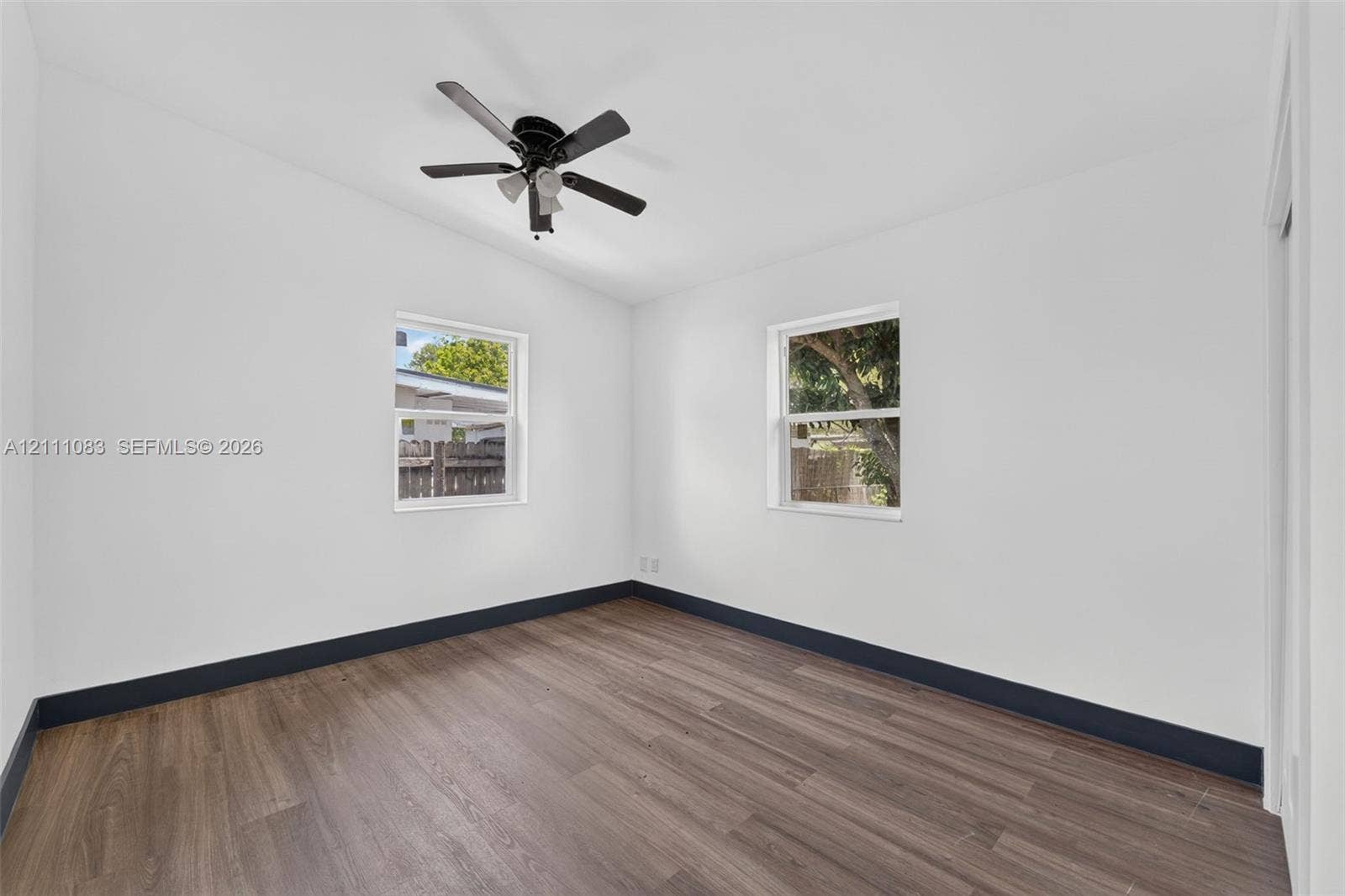 Interior room featuring wood-finish flooring, two dual-pane windows, and a ceiling fan with integrated lighting