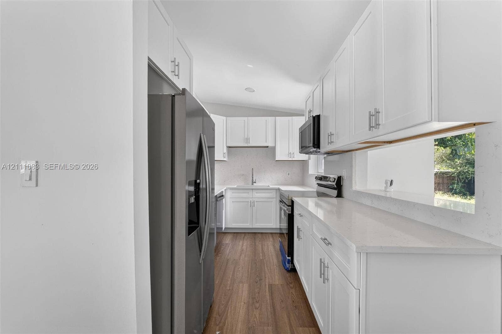 Kitchen featuring white shaker-style cabinetry, solid-surface countertops, wood-finish flooring, and stainless steel appliances
