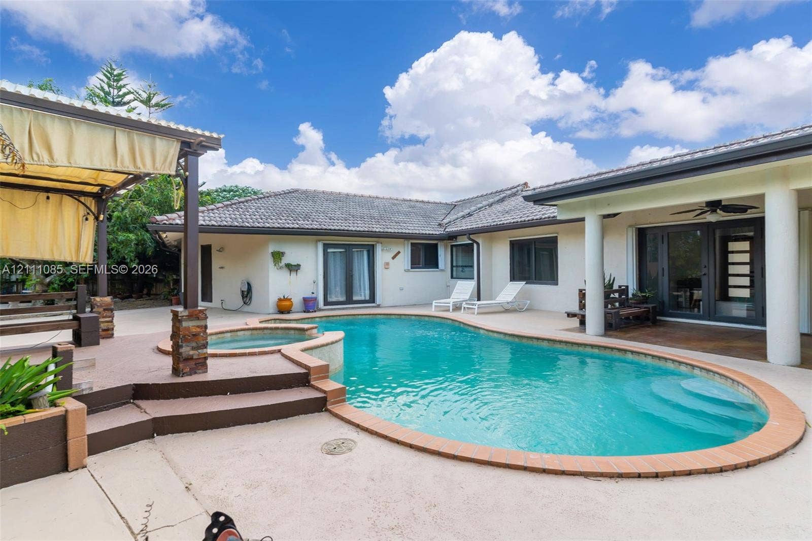 Outdoor swimming pool with integrated spa, concrete patio, covered lanai, and wood-frame pergola