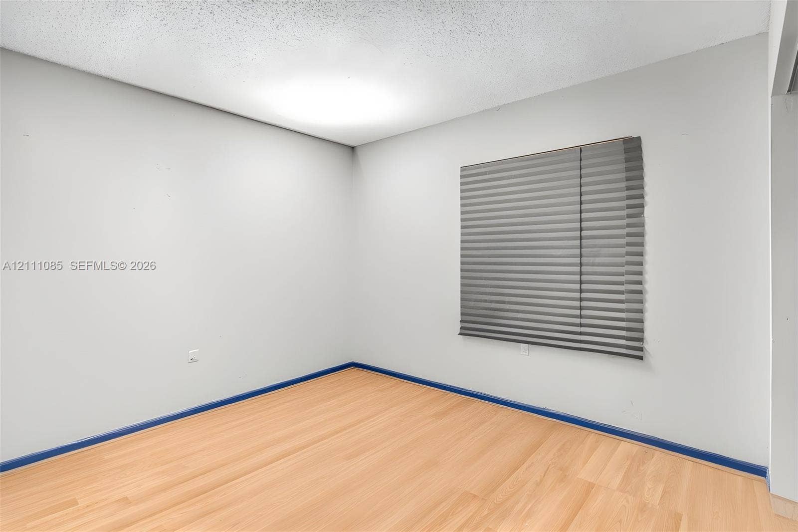 Interior space featuring light-toned wood-finish flooring, neutral wall coloring, and a window with horizontal blinds
