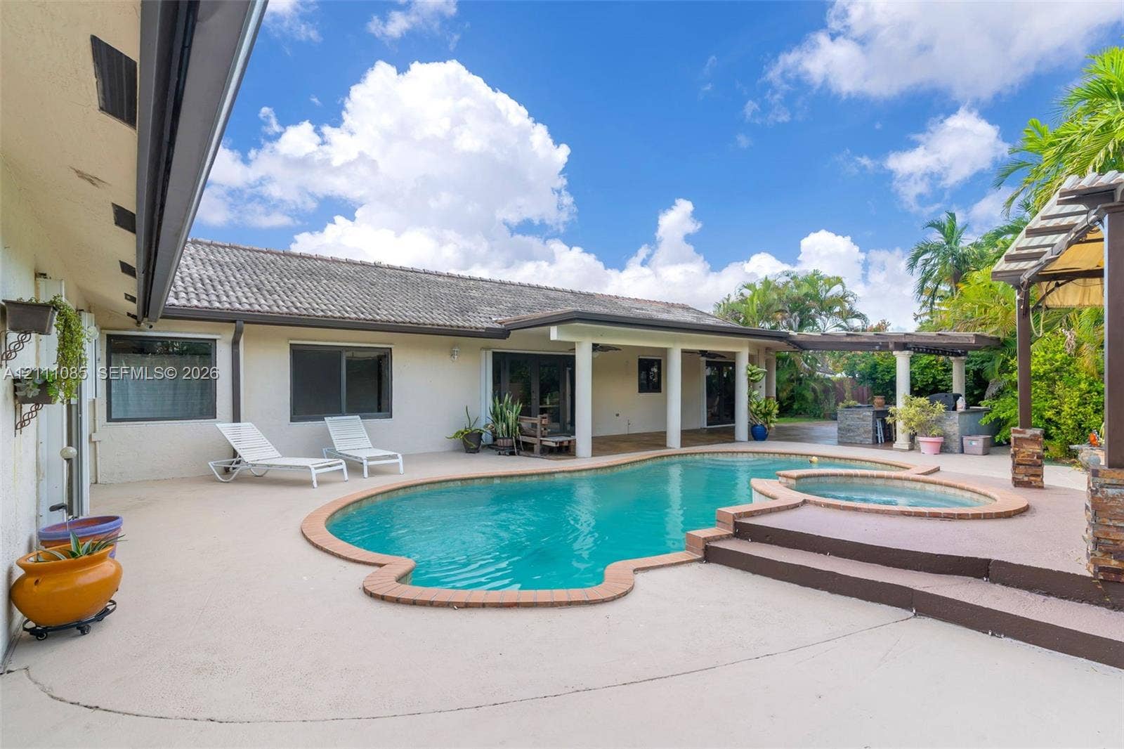 In-ground swimming pool with an integrated spa, concrete patio, and a covered lanai featuring support columns