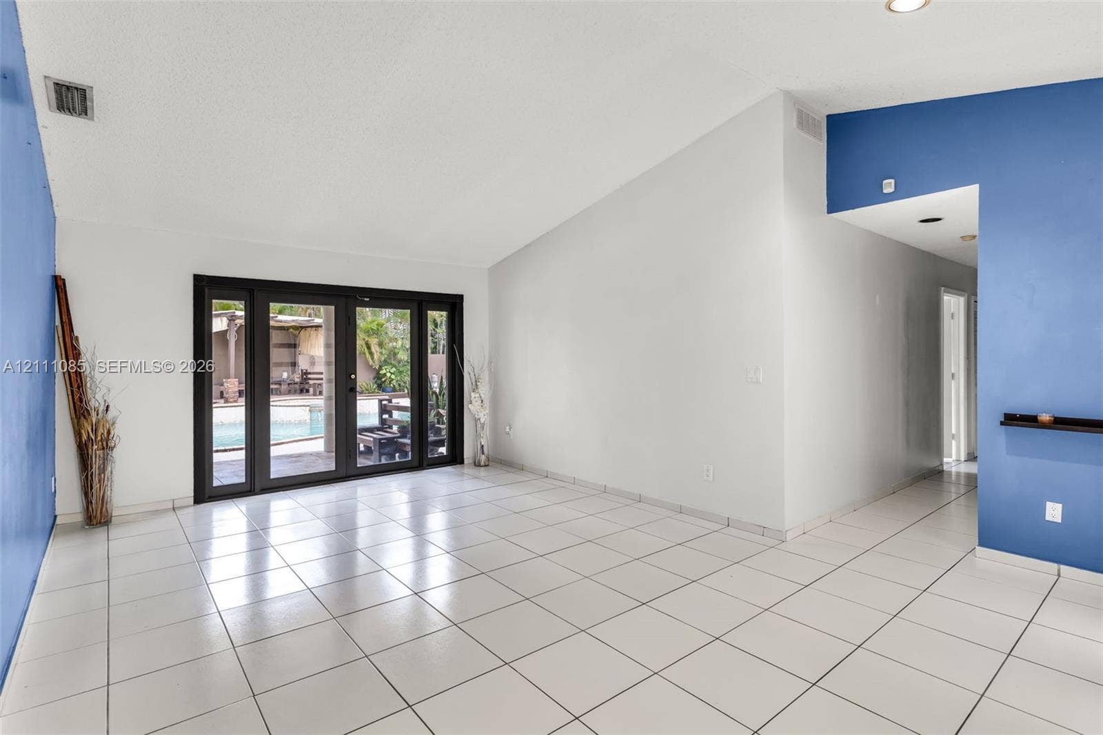 Living area featuring vaulted ceilings, oversized white tile flooring, recessed lighting, and multi-panel sliding glass doors providing outdoor access