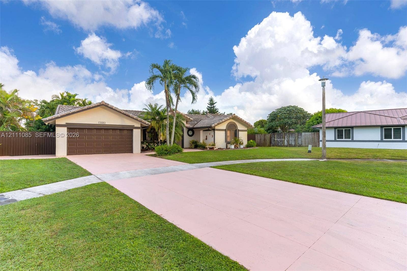 Single-story residence featuring a multi-gabled tiled roof, attached two-car garage, expansive paved driveway, and mature landscaping