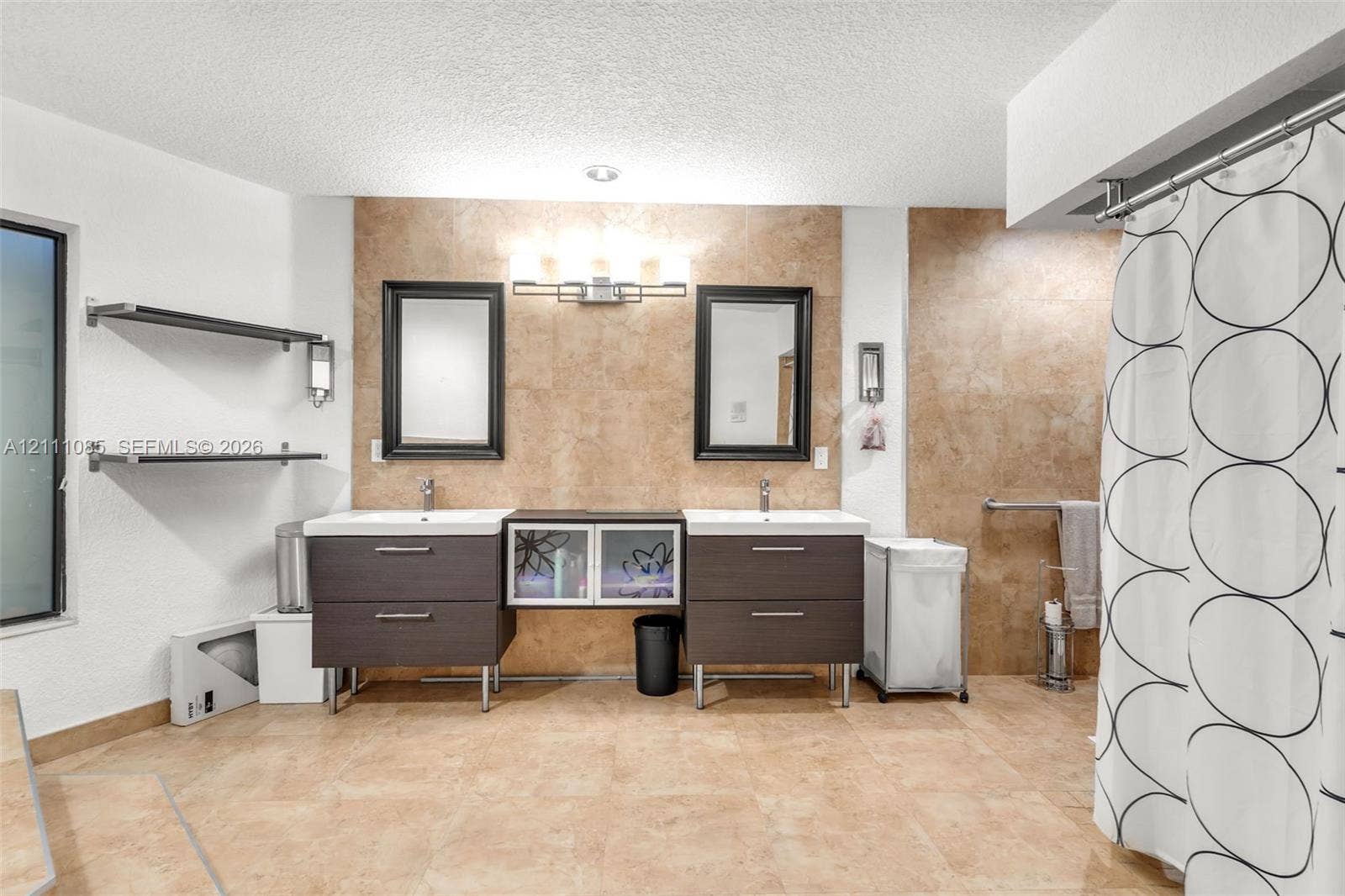 Dual floating vanities featuring dark cabinetry, rectangular sinks, and integrated center storage, complemented by stone-tile wall surfacing, dual framed mirrors, and wall-mounted light fixtures