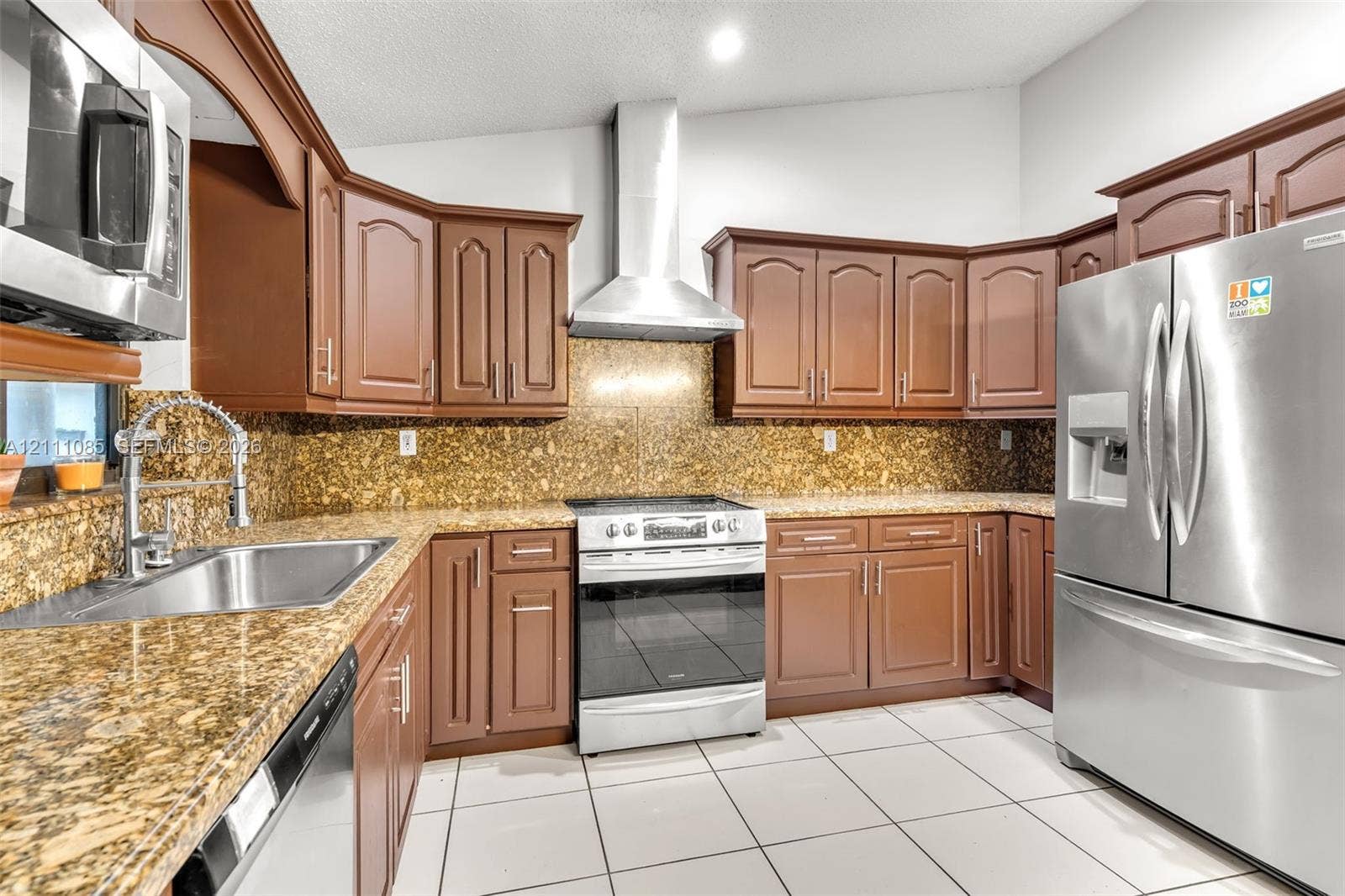 Kitchen featuring stained wood cabinetry, stone-finish countertops, stainless steel appliances, a chimney-style range hood, and tile flooring