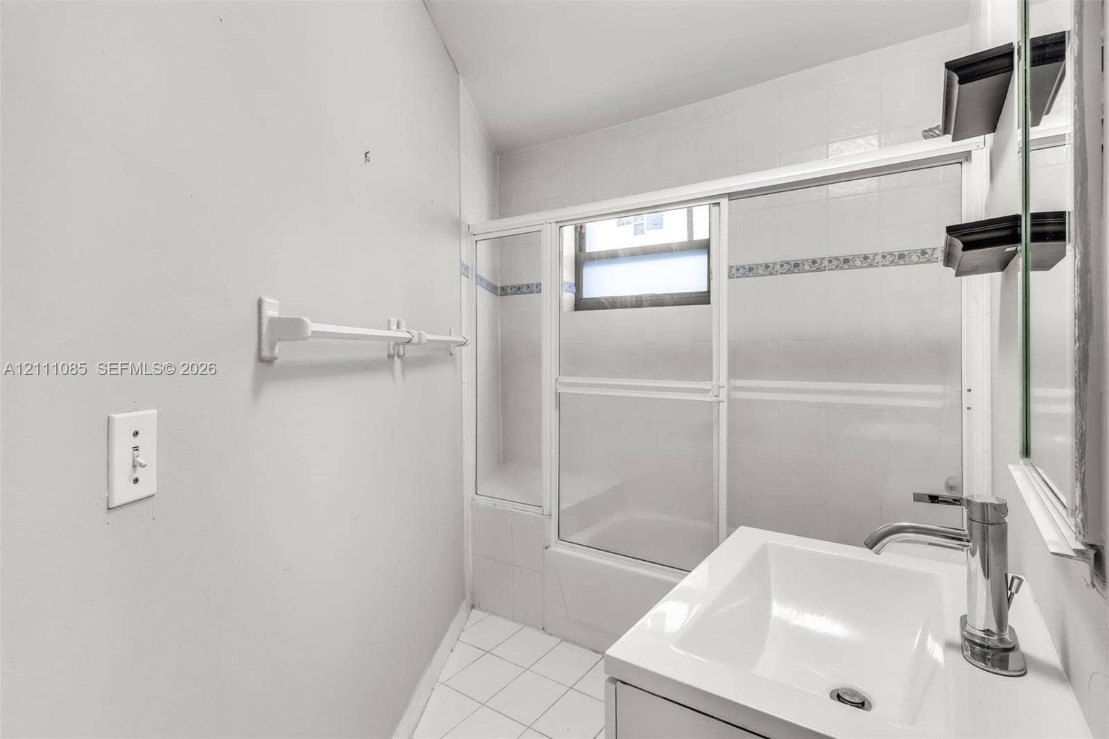 Bathroom featuring a single-basin vanity with a metal faucet, tile flooring, and a tub-shower combination enclosed by sliding glass doors