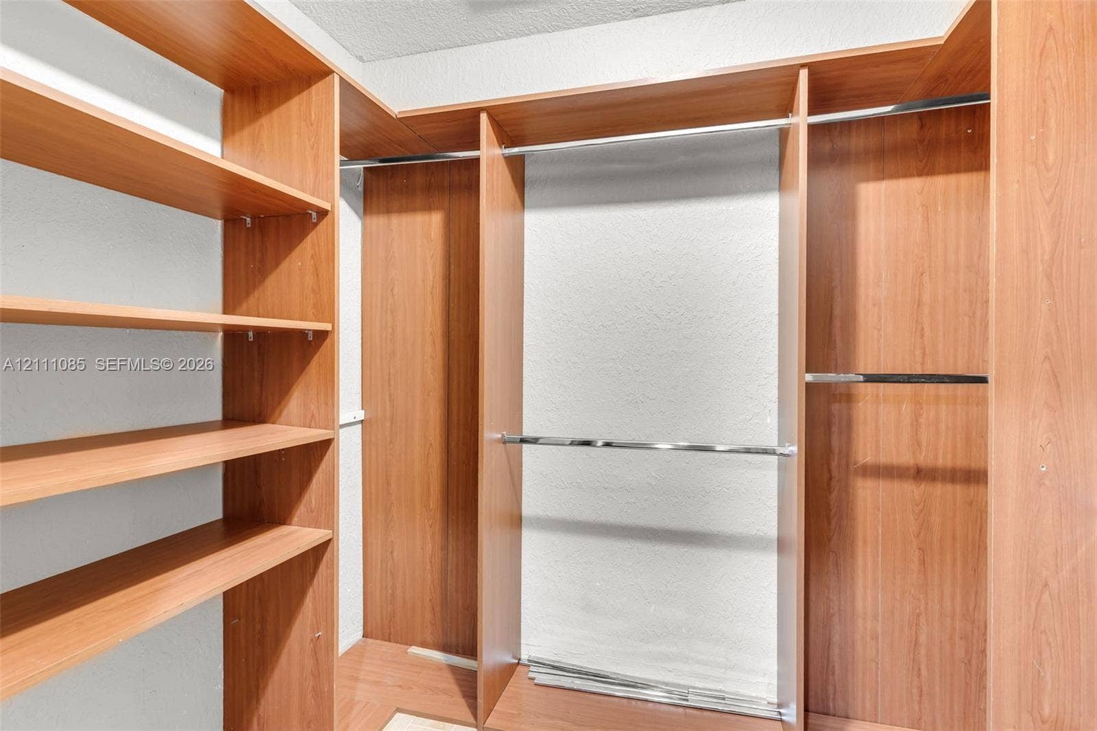 Walk-in closet featuring wood-finish cabinetry, extensive built-in shelving, and dual chrome hanging rods
