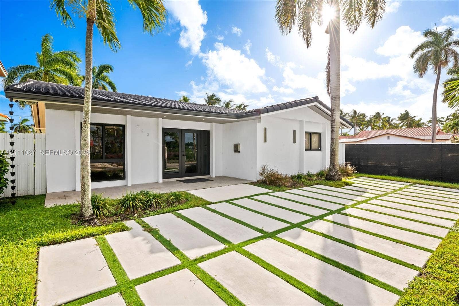822 Polk Street, Hollywood, FL 33019 Single-story exterior featuring white stucco siding, a tiled roof, a geometric concrete paver driveway, double glass entry doors, and large-format window frames