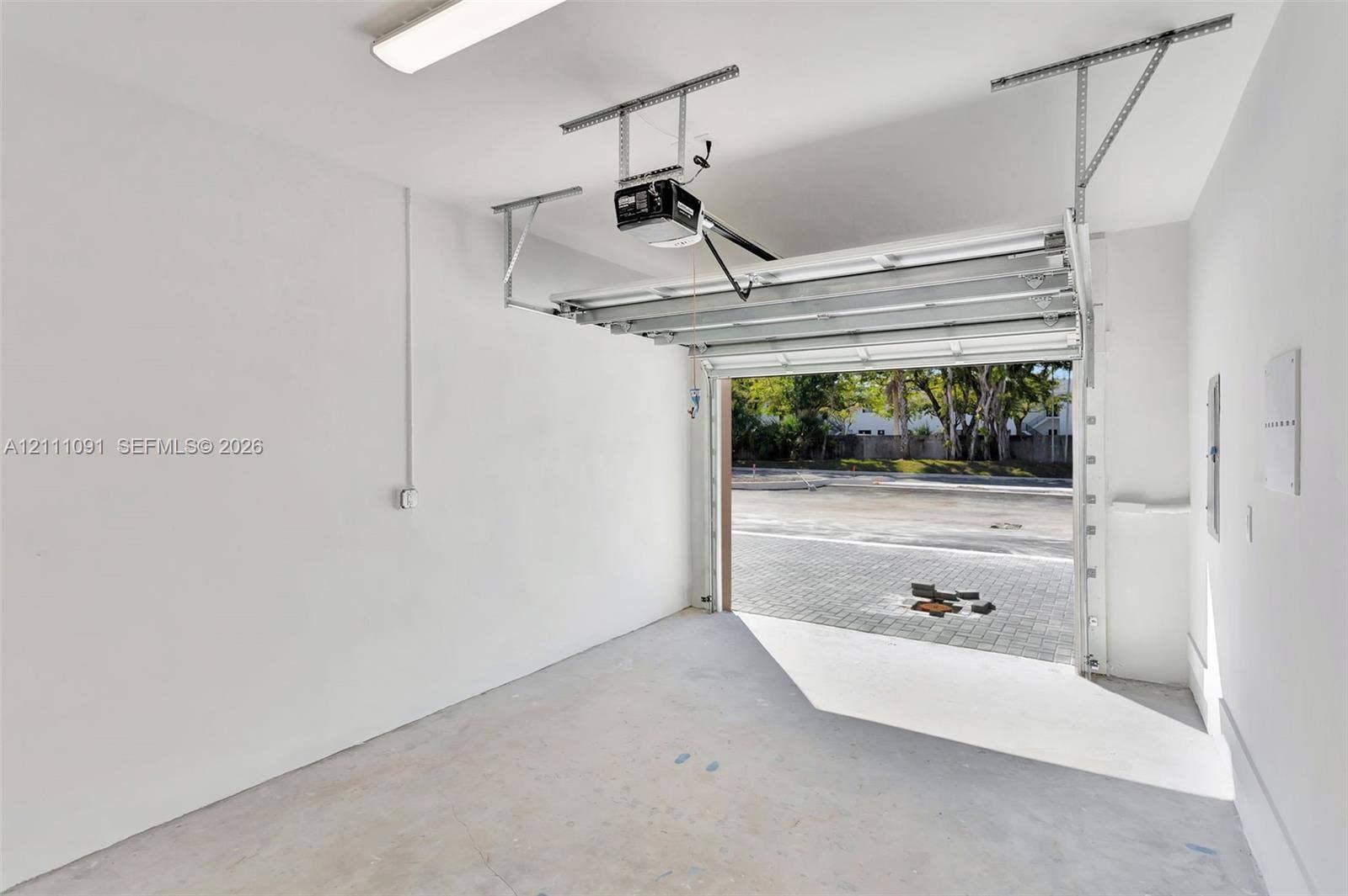 Enclosed garage featuring painted interior walls, smooth concrete flooring, overhead lighting, and an automated garage door opener
