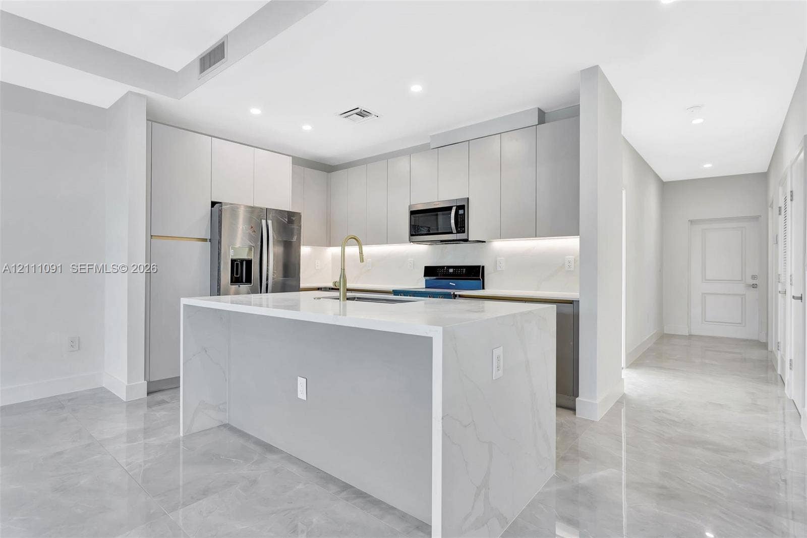 Modern kitchen featuring flat-panel cabinetry, a waterfall-edge stone island, polished tile flooring, stainless steel appliances, and under-cabinet lighting
