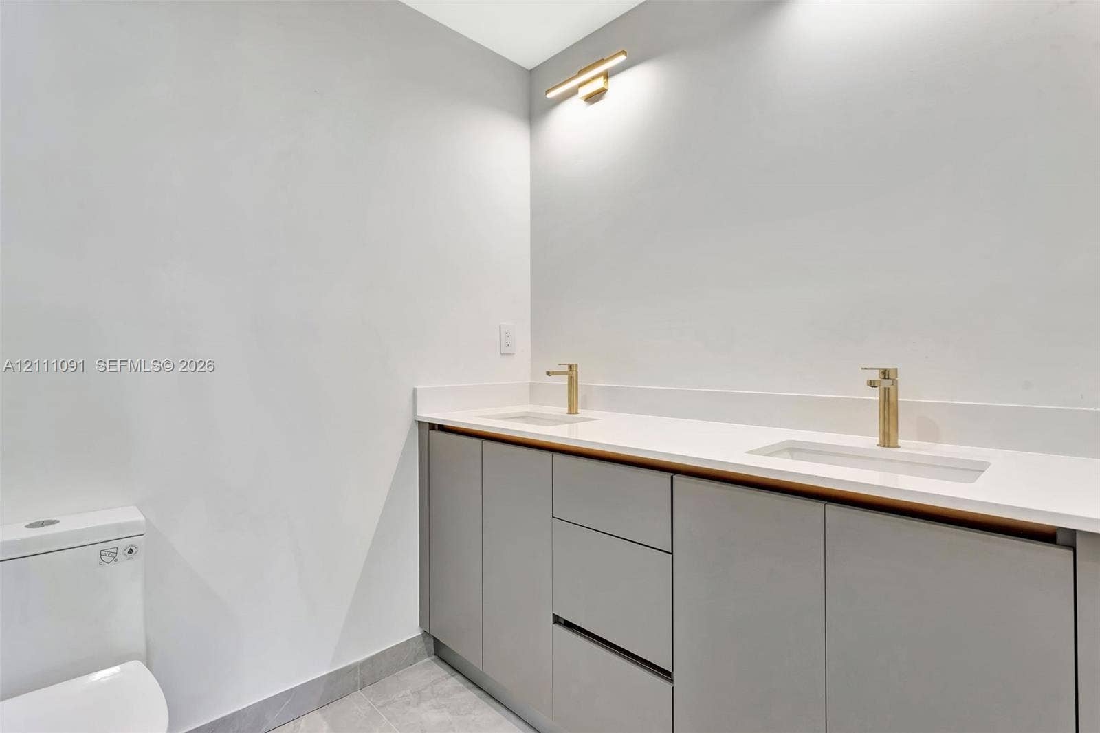 Dual-sink vanity with light-colored solid surface countertop, metallic finish faucets, flat-panel gray cabinetry, and horizontal wall-mounted lighting