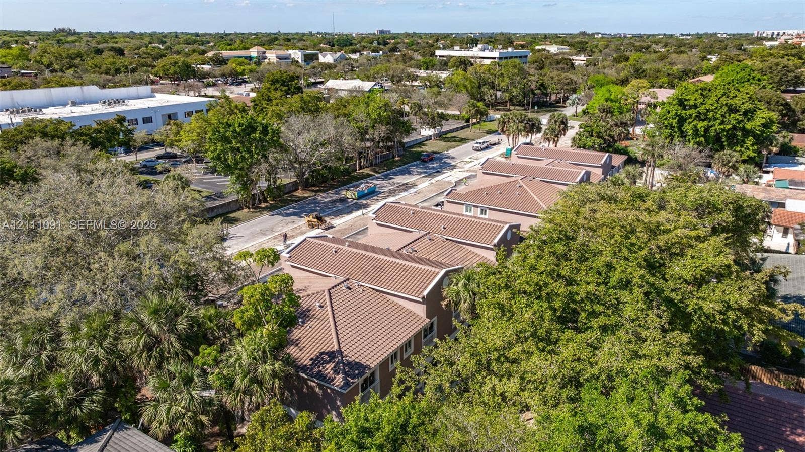Aerial perspective featuring a multi-unit complex with neutral-toned stucco exteriors and metal roofing, positioned among established landscaping and mature trees
