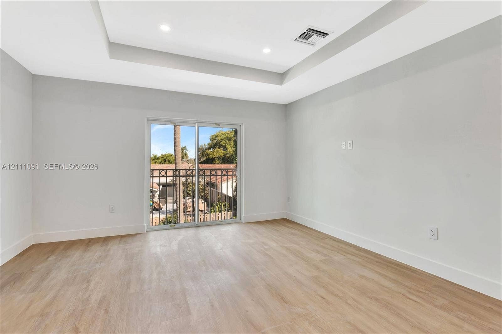 Tray ceiling with recessed lighting, wood-finish flooring, and sliding glass door with wrought iron balcony railing