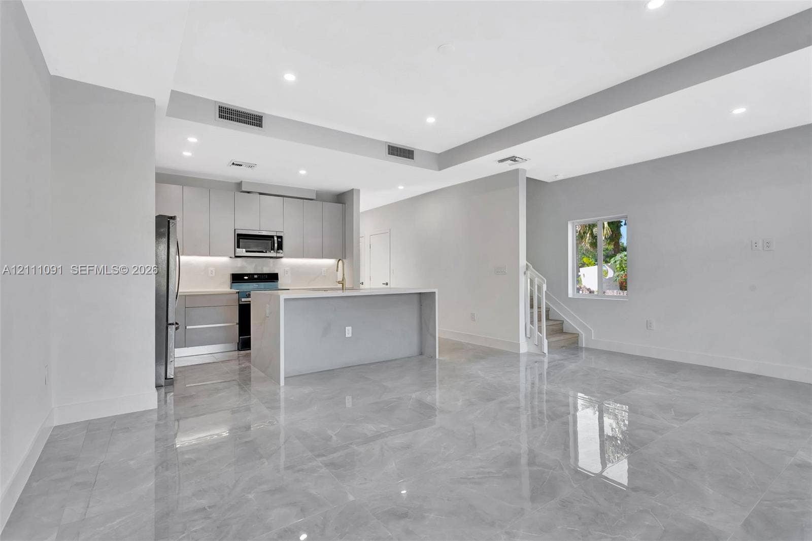 Open-concept kitchen featuring flat-panel cabinetry, a waterfall-edge island, polished stone-finish flooring, and recessed ceiling lighting