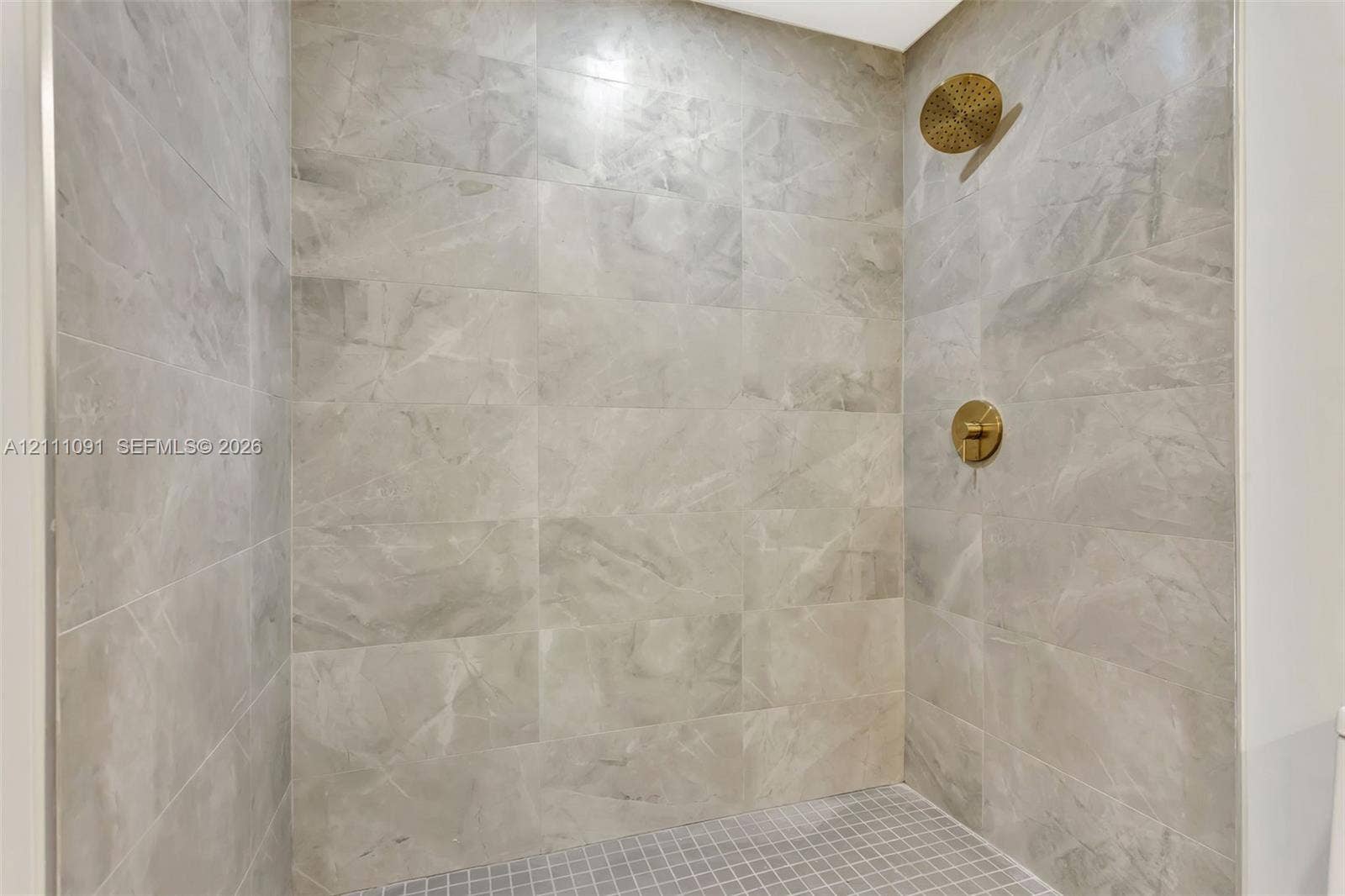 Walk-in shower featuring large-format stone-finish wall tile, a mosaic tile floor, and brushed-gold hardware including a rainfall showerhead and wall-mounted control