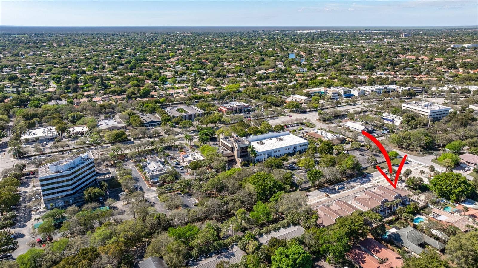 Aerial perspective of a multi-unit property featuring a tile roof, paved parking area, and mature landscaping