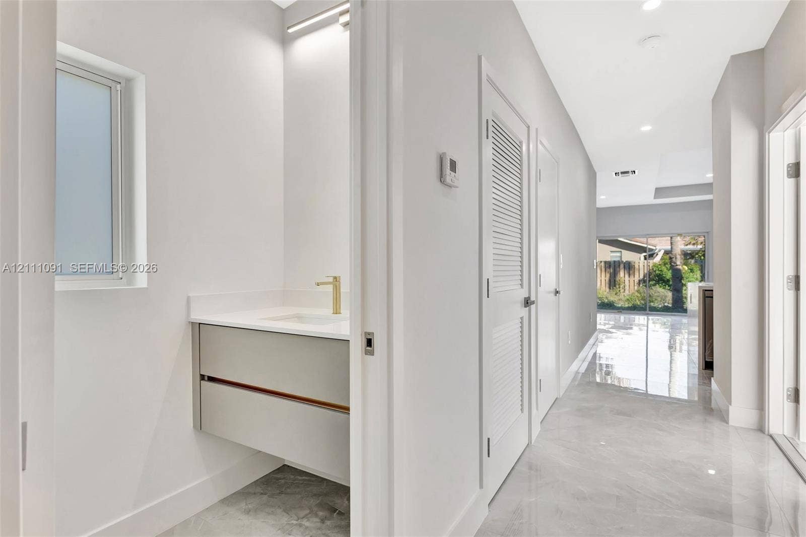 Floating vanity with integrated countertop and gold-tone faucet, complemented by stone-finish tile flooring and recessed lighting throughout