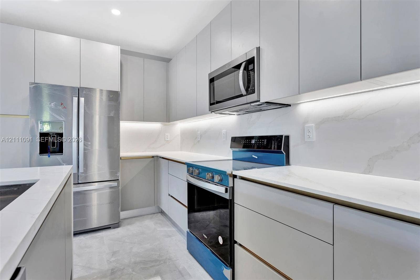 Kitchen featuring flat-panel cabinetry, stone-surface countertops, full-height stone backsplash, under-cabinet lighting, and stainless steel appliances