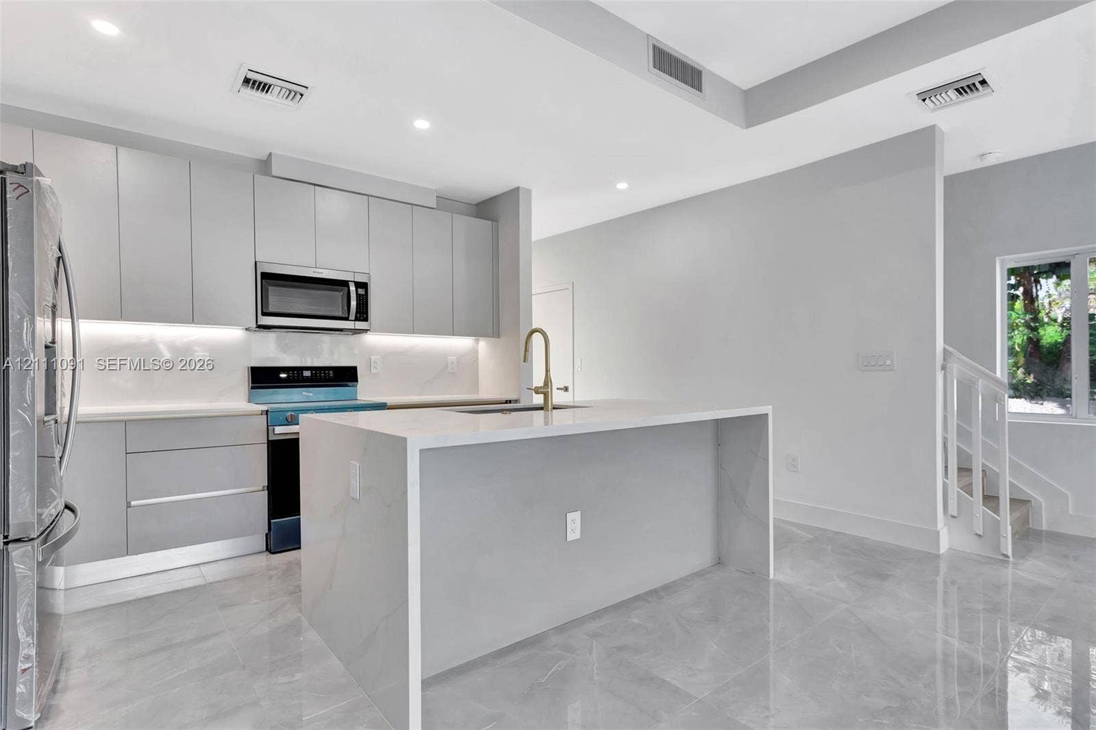 Contemporary kitchen featuring high-gloss cabinetry, a waterfall-edge island, stone-finish countertops, recessed lighting, and large-format tile flooring