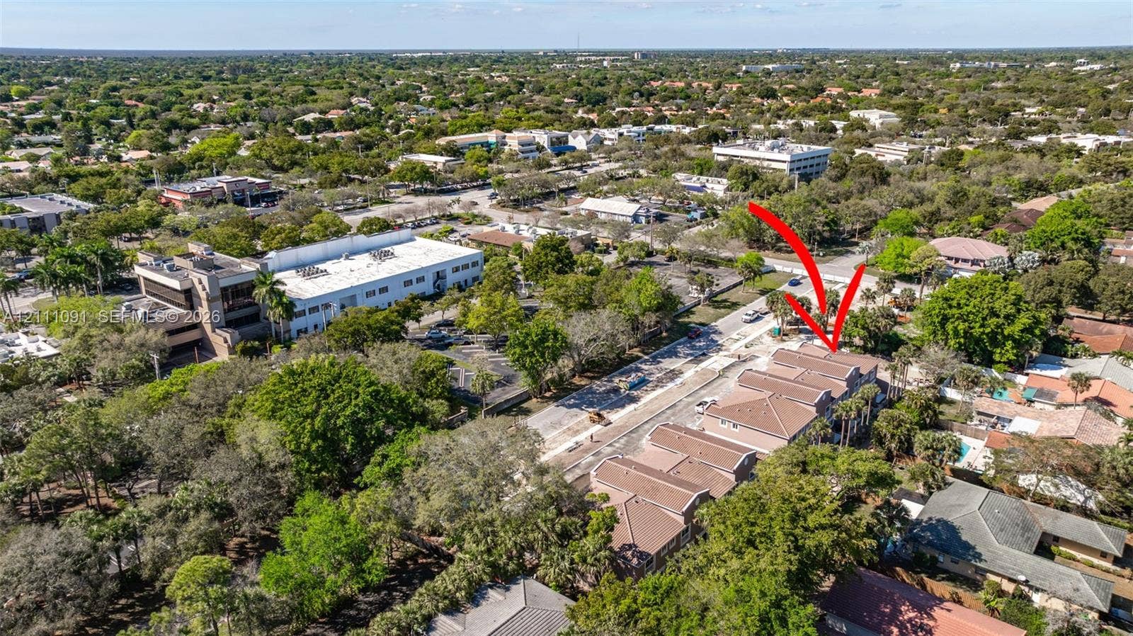 Aerial perspective of a multi-unit property featuring a shingled roof, stucco exterior, paved driveway, and mature landscaping