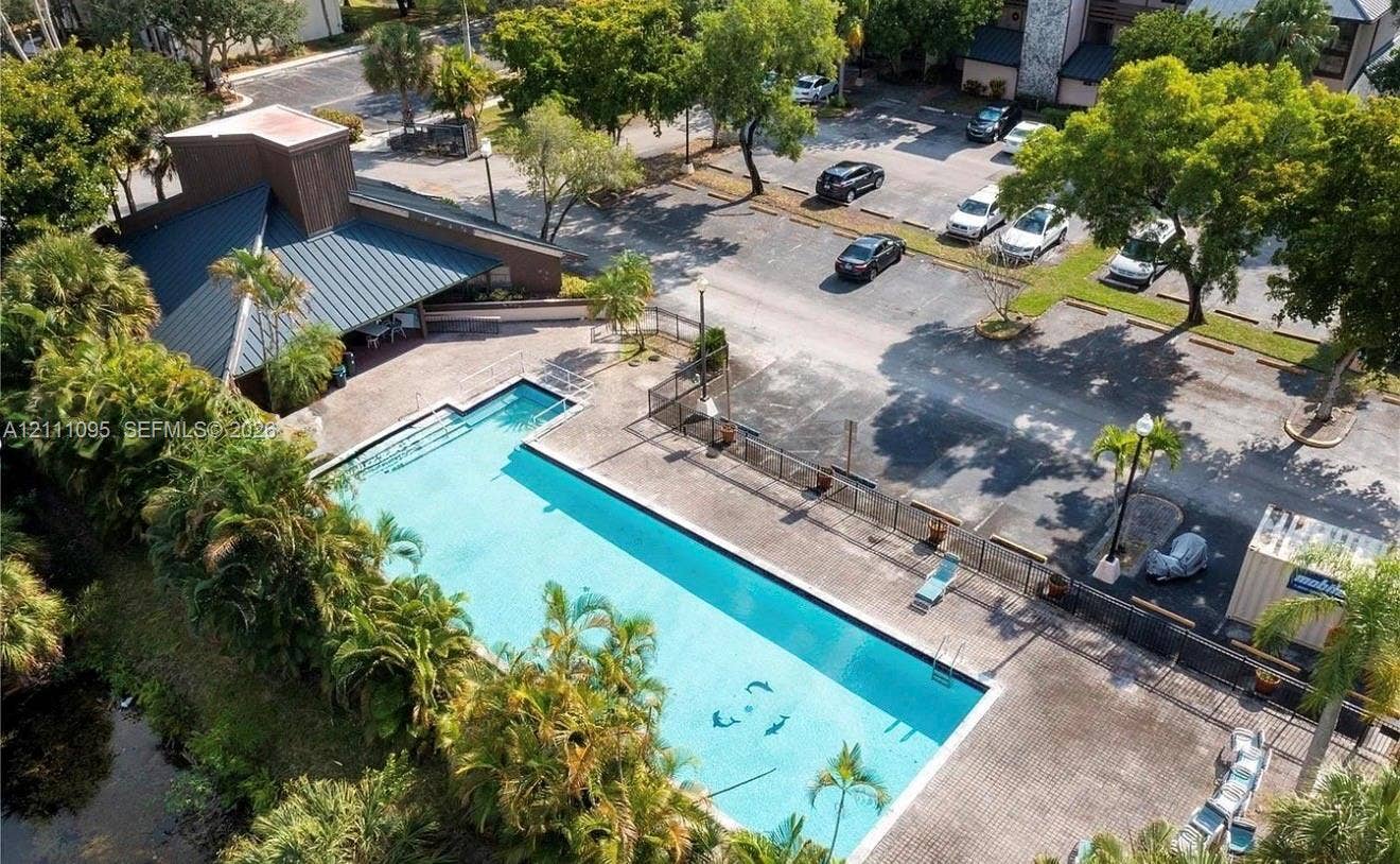 120 SW 96th Terrace, #104, Plantation, FL 33324 Rectangular swimming pool featuring a paved pool deck, metal perimeter fencing, covered pavilion, and mature tropical landscaping
