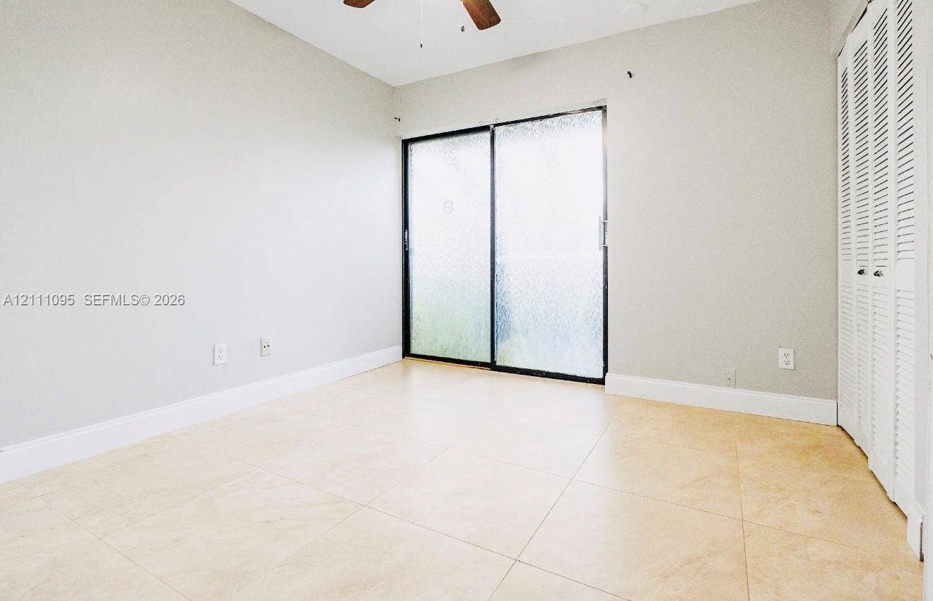 120 SW 96th Terrace, #104, Plantation, FL 33324 Interior space featuring oversized neutral tile flooring, sliding glass doors, white louvered-style closet doors, and a ceiling fan