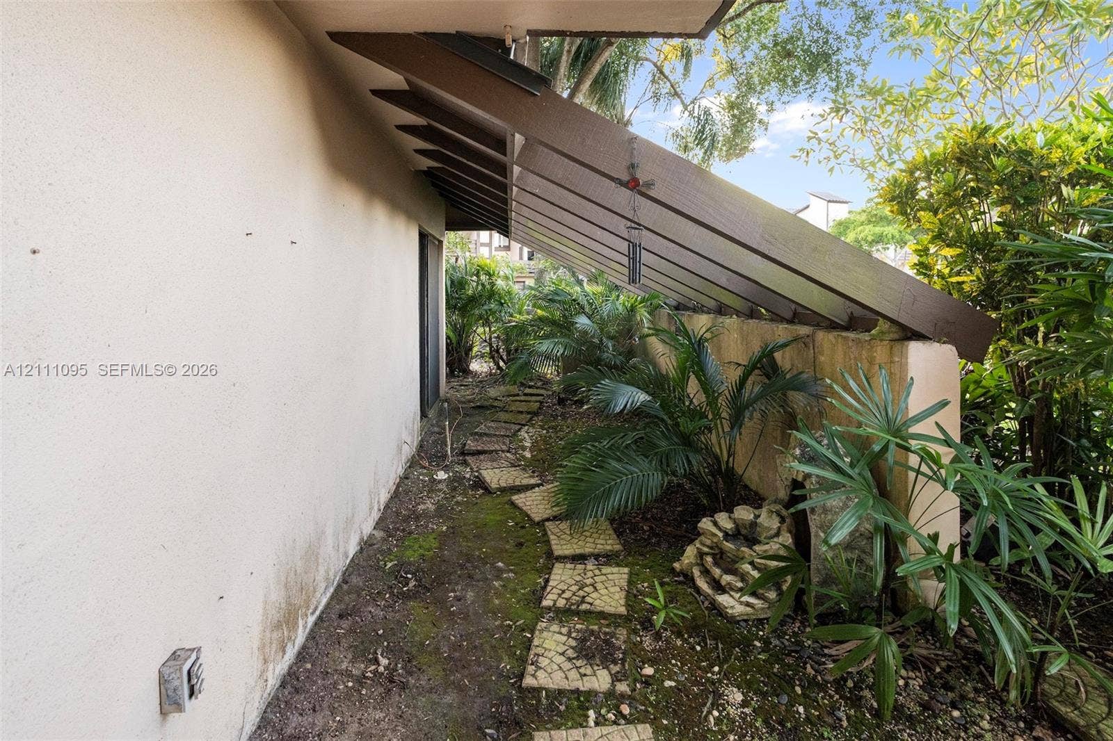 120 SW 96th Terrace, #104, Plantation, FL 33324 Side exterior featuring an extended shed roof with exposed rafter tails, stone paver walkway, and mature landscaping
